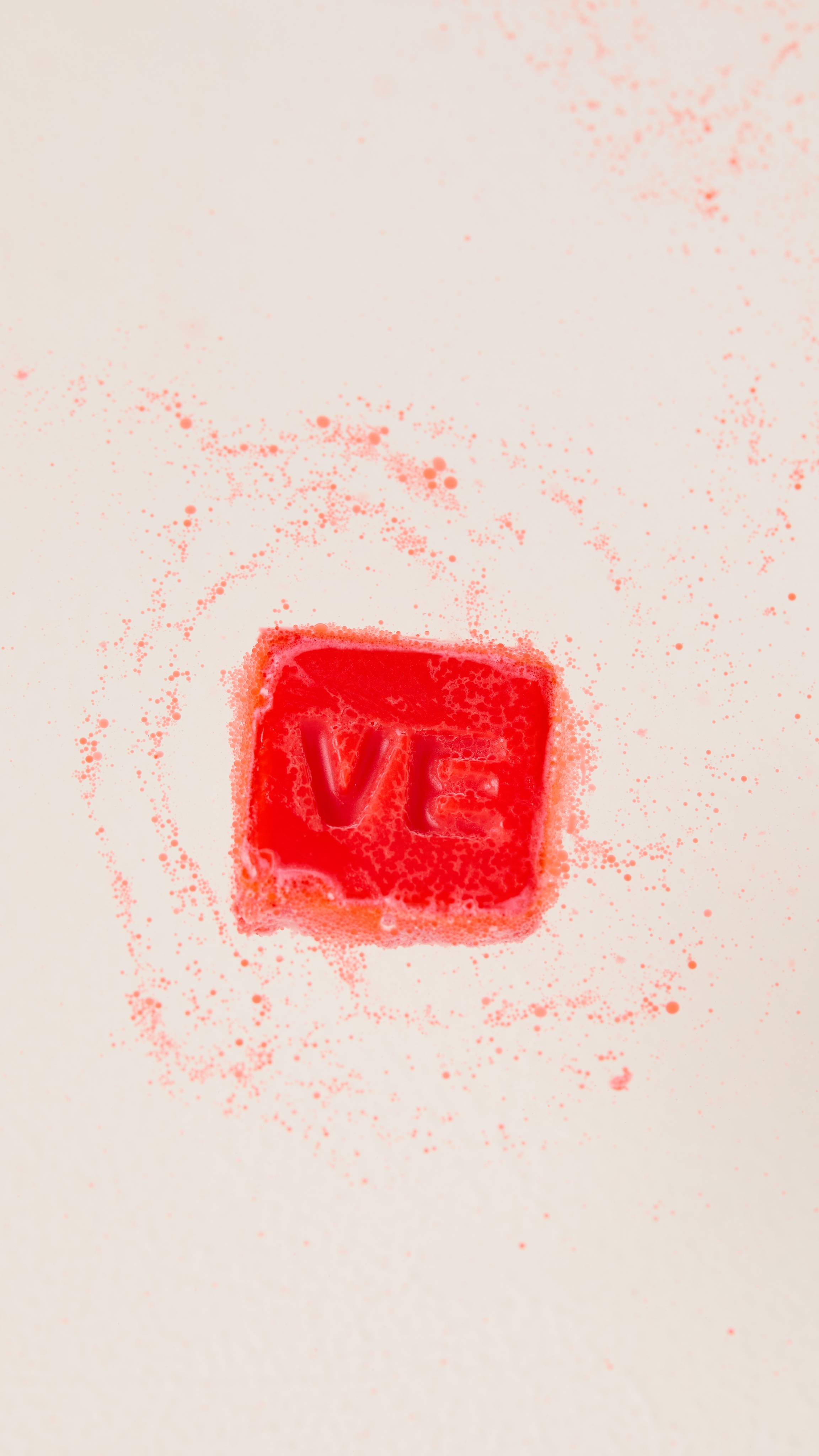 The image shows a single square of the deep red Love Spell Lush Melt as it begins to melt in the bath water. 