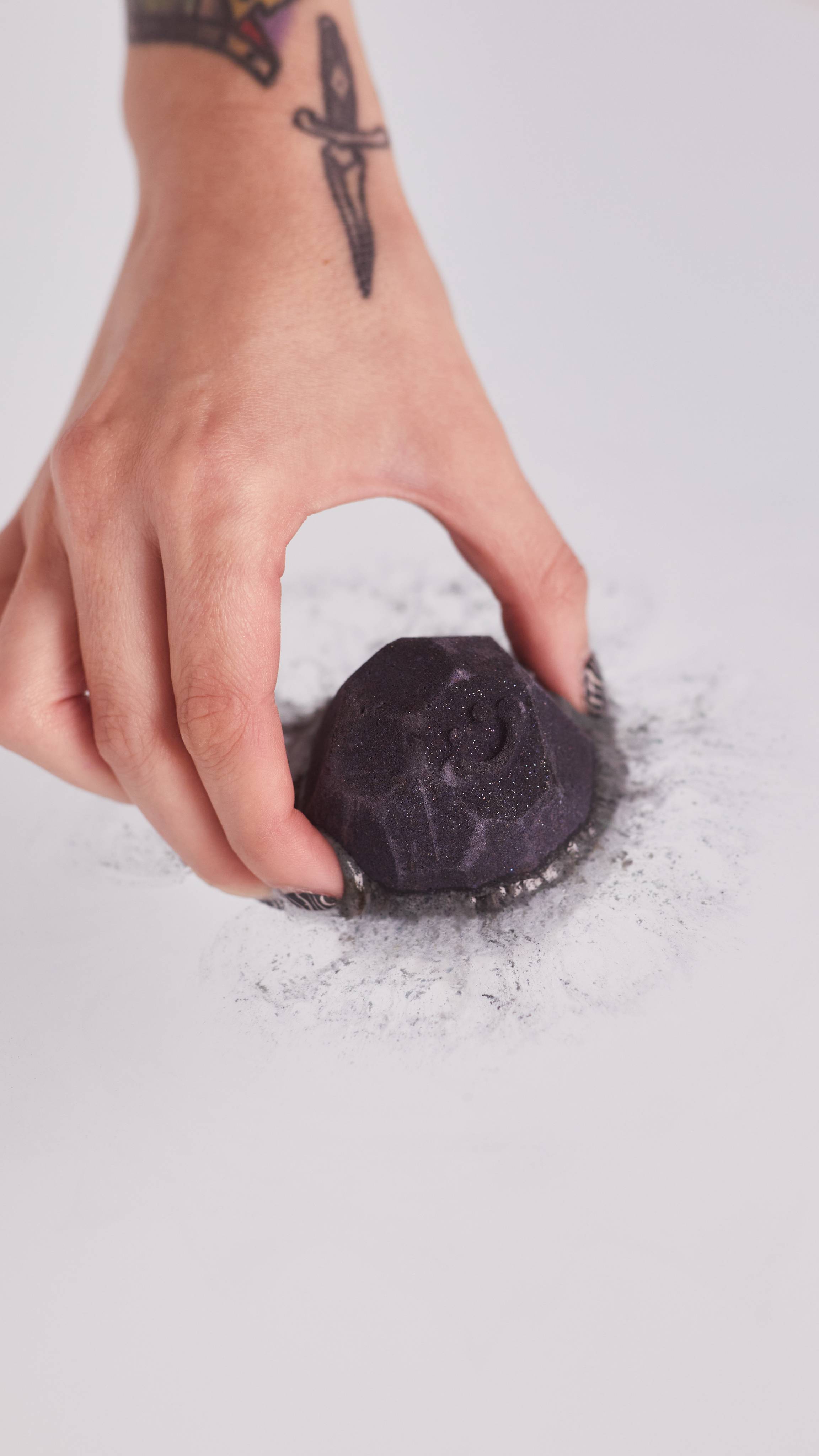 Image shows a close-up of the model placing the Lump of Coal bath bomb into the water with the black beginning to bleed out. 