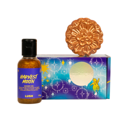 Luna Serenade gift. A small bottle of glittery golden Lush "Harvest Moon" shower gel stands beside a purple and blue starry gift box. Atop the box rests a bronze, intricately patterned, mooncake-shaped bath bomb