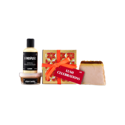 A "Lush Celebrations" gift box wrapped in red and gold geometric paper with an orange ribbon and red tag, flanked by S'mores shower gel, Sticky Dates body scrub, and a slice of soap.