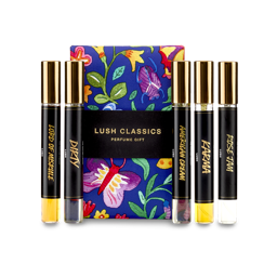 The image shows a "LUSH CLASSICS" perfume gift set. Five thin, cylindrical glass perfume bottles with amber and clear liquids inside are arranged around a dark blue box featuring vibrant floral and butterfly illustrations.