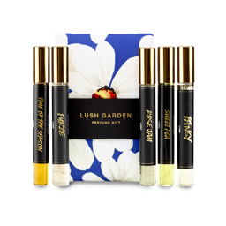 The image shows a "LUSH GARDEN" perfume gift set. Five thin, cylindrical glass perfume bottles with amber and clear liquids are arranged around a dark blue box featuring a large white floral design.