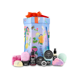 The image shows the 'Lush Life' gift set. A tall, hexagonal gift box with colourful illustrations sits behind a selection of 12 products, including bath bombs, soap, and potted products. 