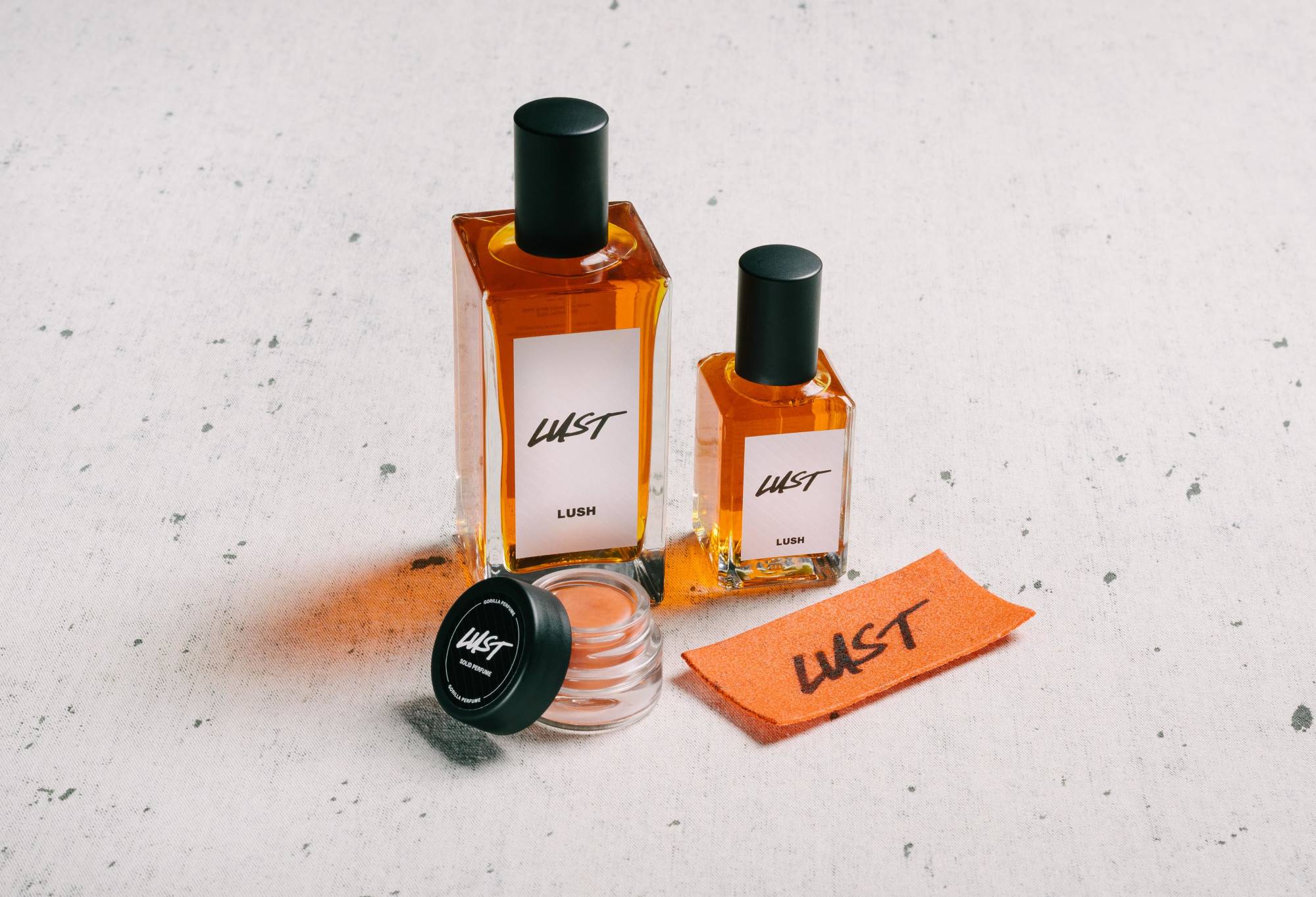 The whole Lust fragrance collection is displayed on a white surface, flecked with grey.