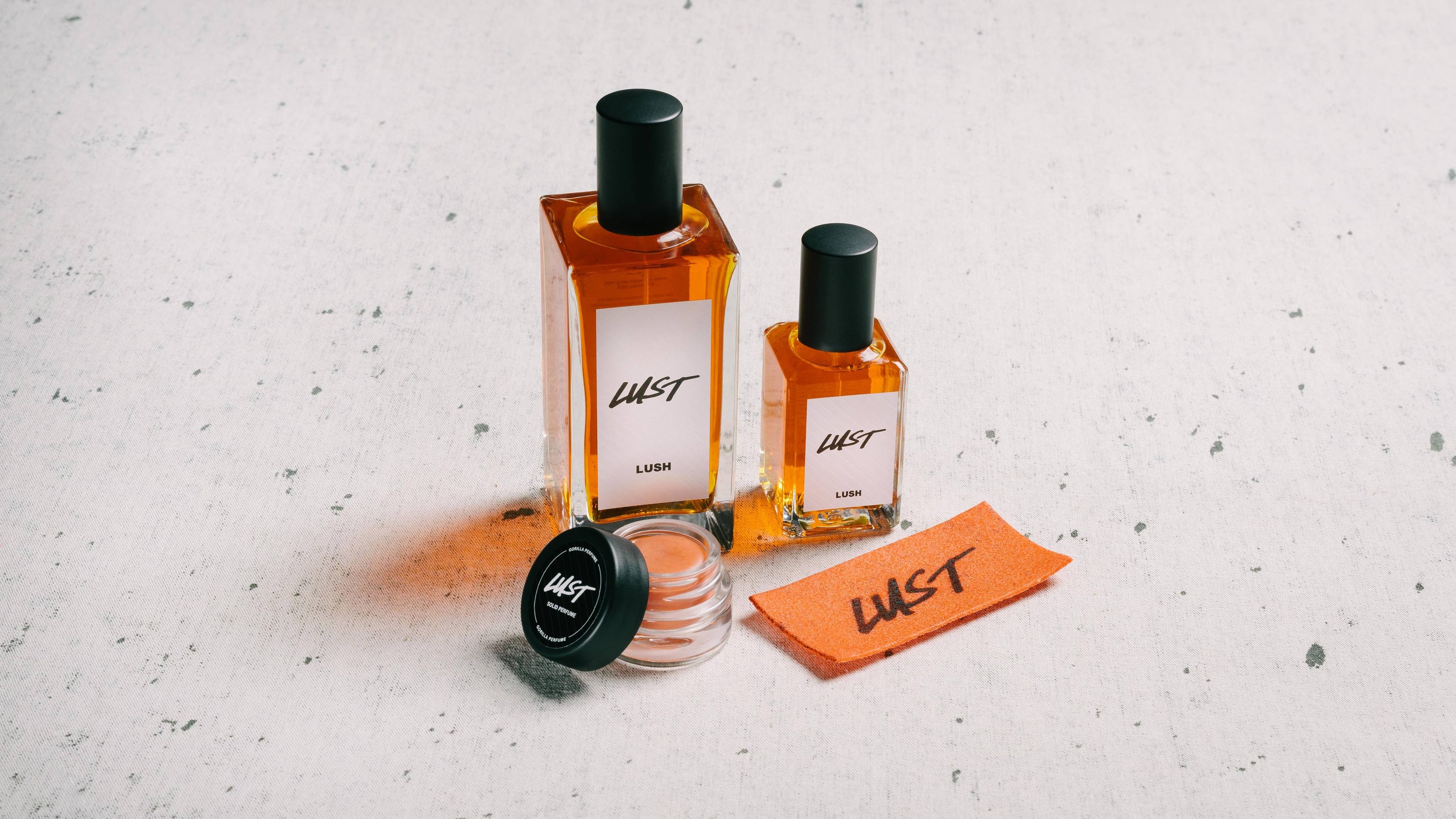 The whole Lust fragrance collection is displayed on a white surface, flecked with grey.