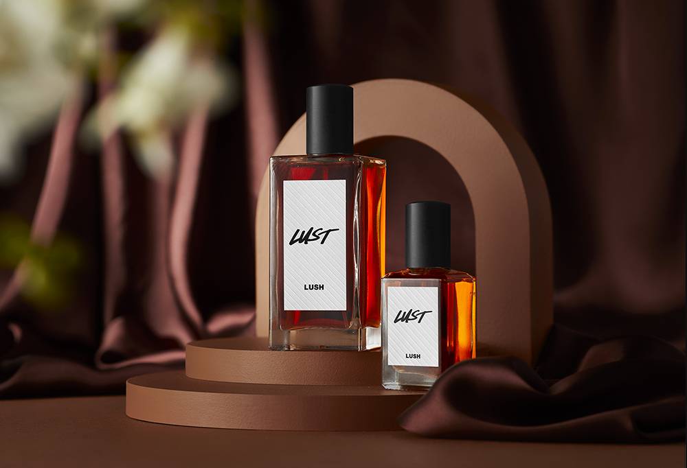 Lust perfume is placed on an curved brown podium and background. Behind is dimly lit with smoke drifting towards the bottles.