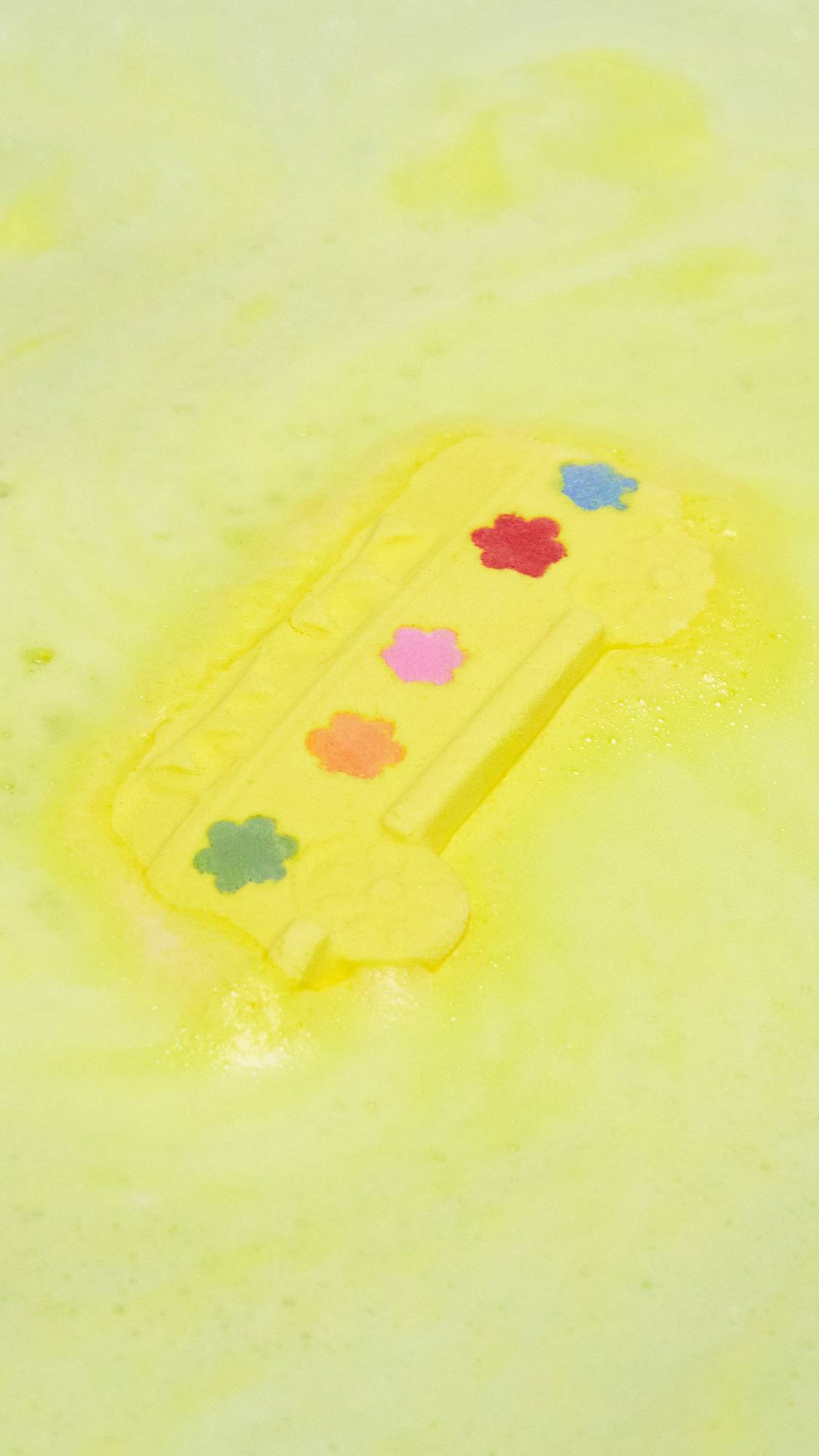 The Magic Bus bath bomb is sat in the bath water, still intact, giving off a thick velvety blanket of canary-yellow foam. 