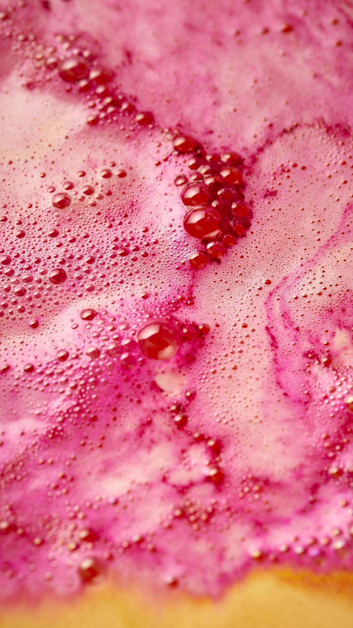 A super-close-up of the bath water after using the festive Magical Santa Sleigh, two-part bath bomb. There is a blanket of brilliantly pink, tiny, foamy bubbles.
