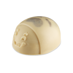Mama-chino Scrubee. A smooth, cream-coloured solid body scrub shaped like a stylised ladybird with a smiling face. The dome-shaped bar features dark, mottled patches on its back.