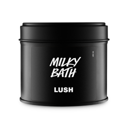 A matte black circular tin with a matching lid. The front label features the Lush logo and the product name "Milky Bath" in bold, white hand-drawn style typography. Set against a plain grey background.