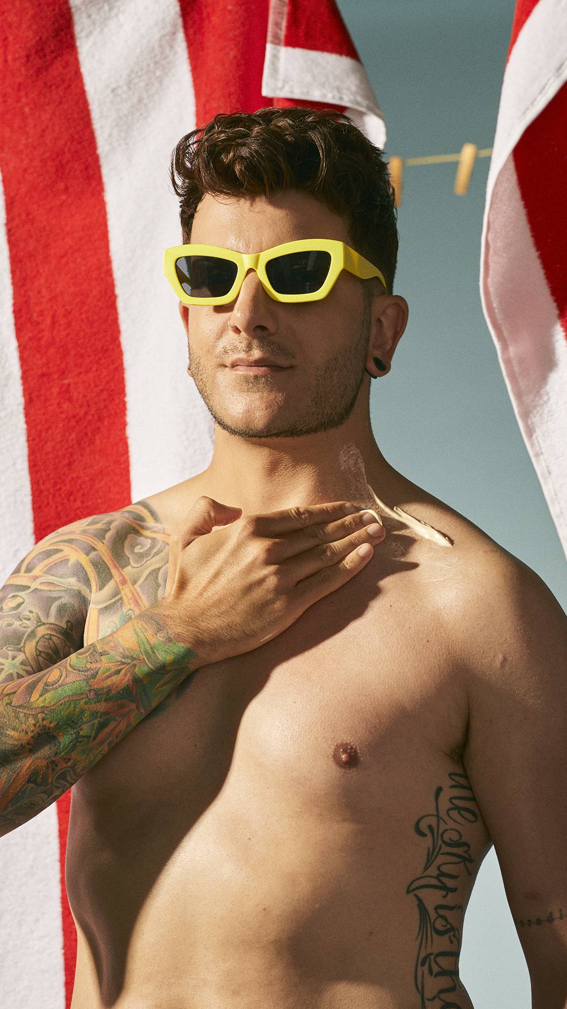 Model is wearing yellow framed sunglasses are they spread the lotion over their neck and chest.