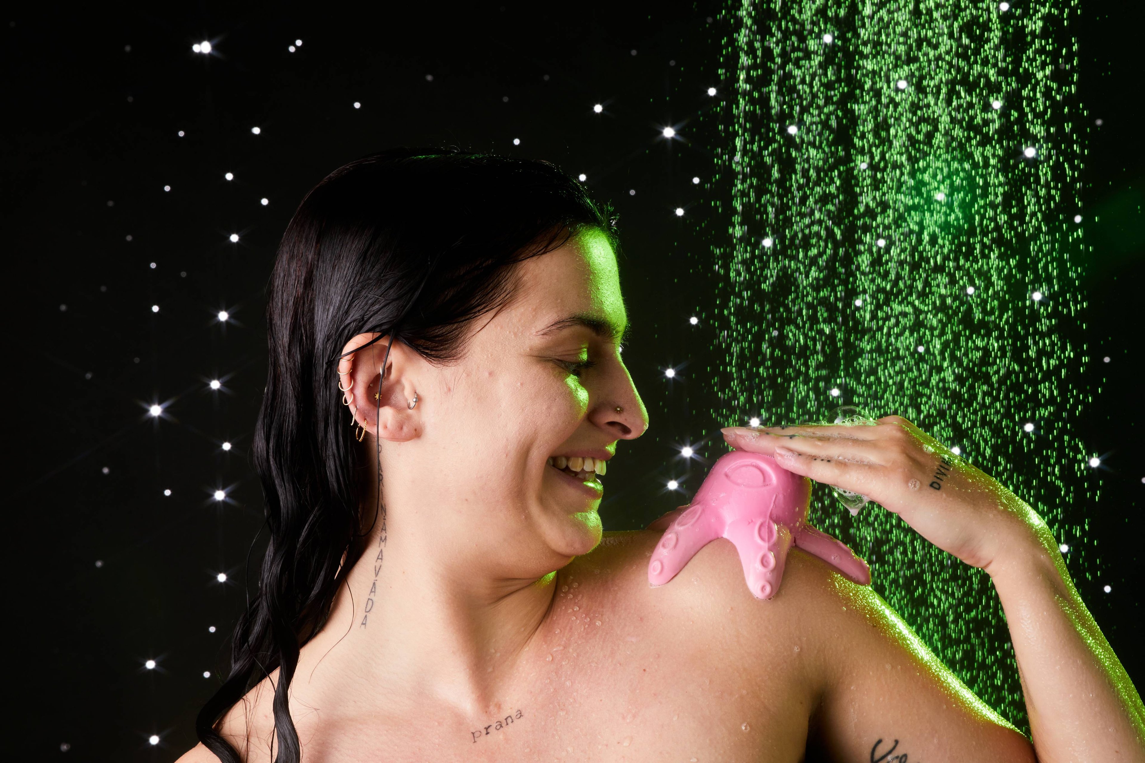 Model is standing under running shower water with the Monster Octopus shower jelly on their shoulder as they smile and pet it.