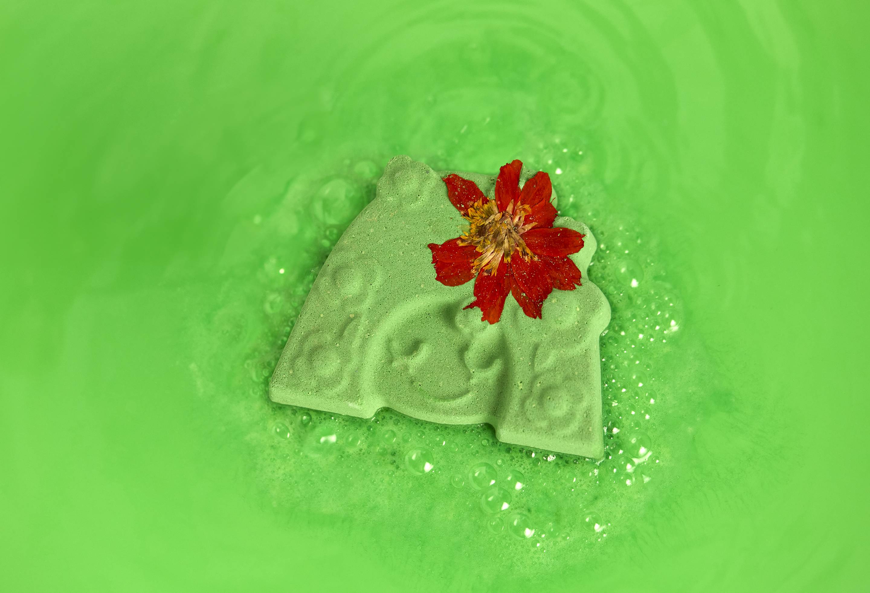 The Mother Nature bath bomb sits, dissolving and creating vibrant, neon-green bath water. 