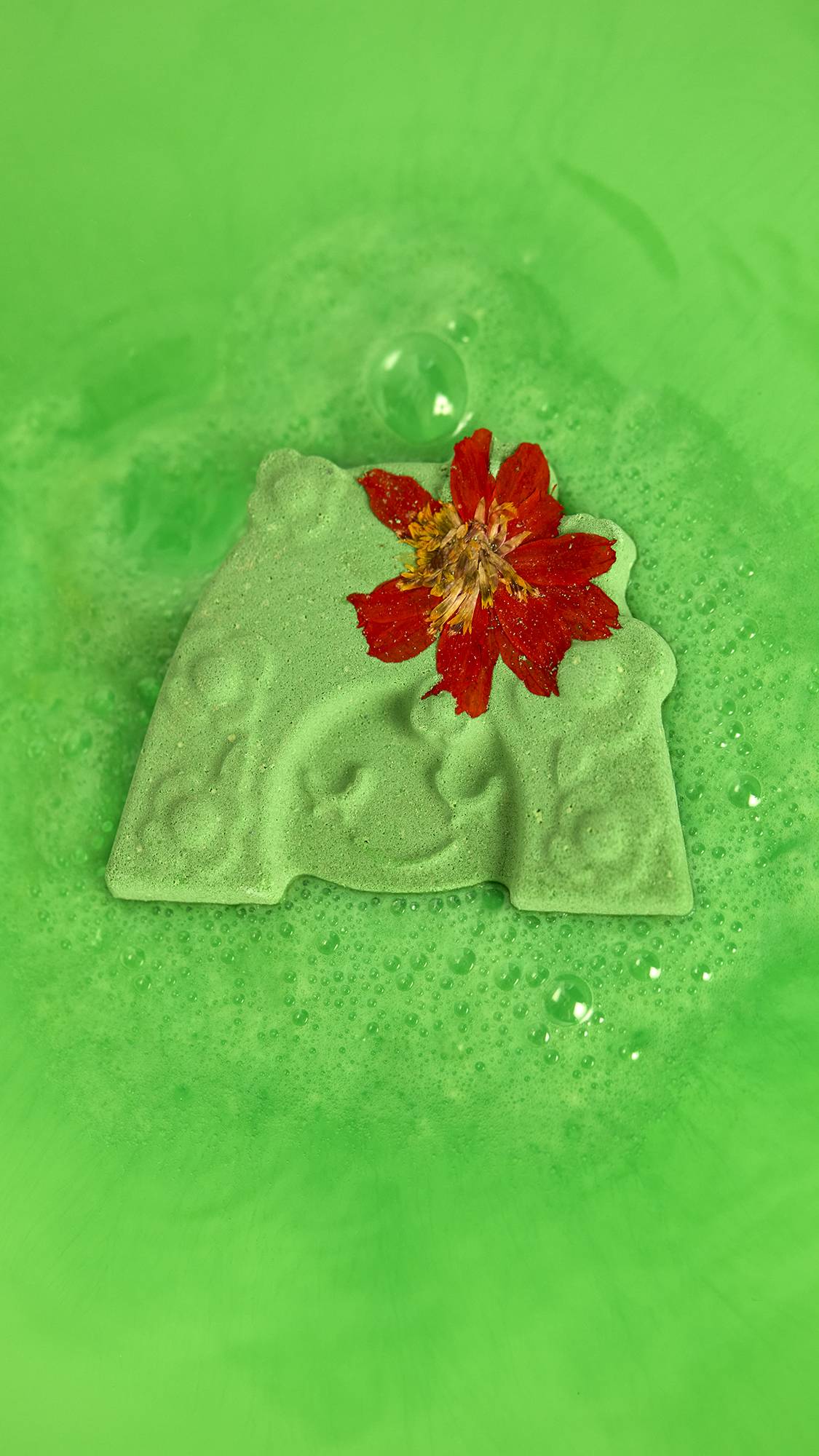 The Mother Nature bath bomb sits, dissolving and creating vibrant, neon-green bath water. 