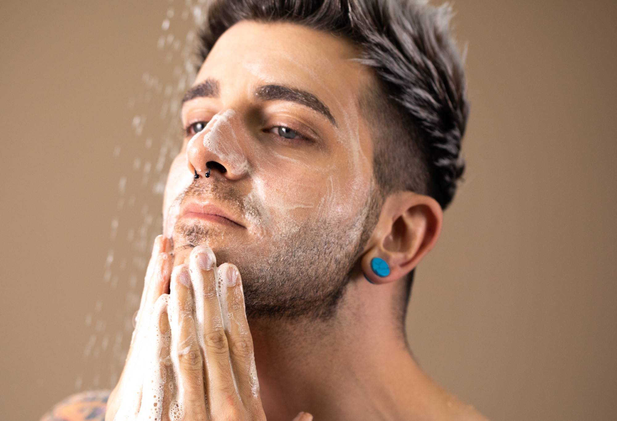 A bearded person's face is covered in whiteish soap suds, which are being rubbed into the chin with both hands.