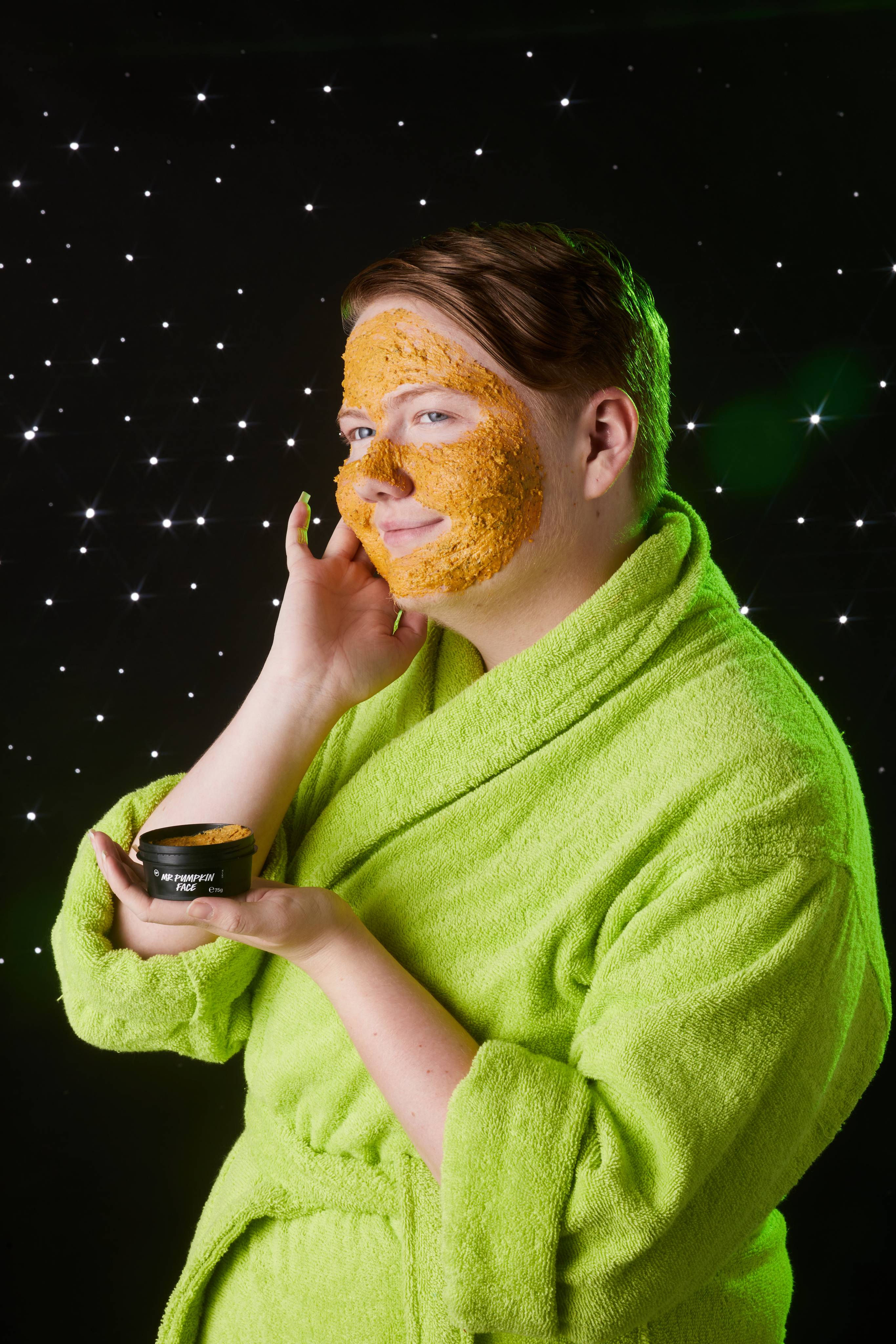 Image shows model in a neon-green robe as they gently spread the product over their face with their hand.