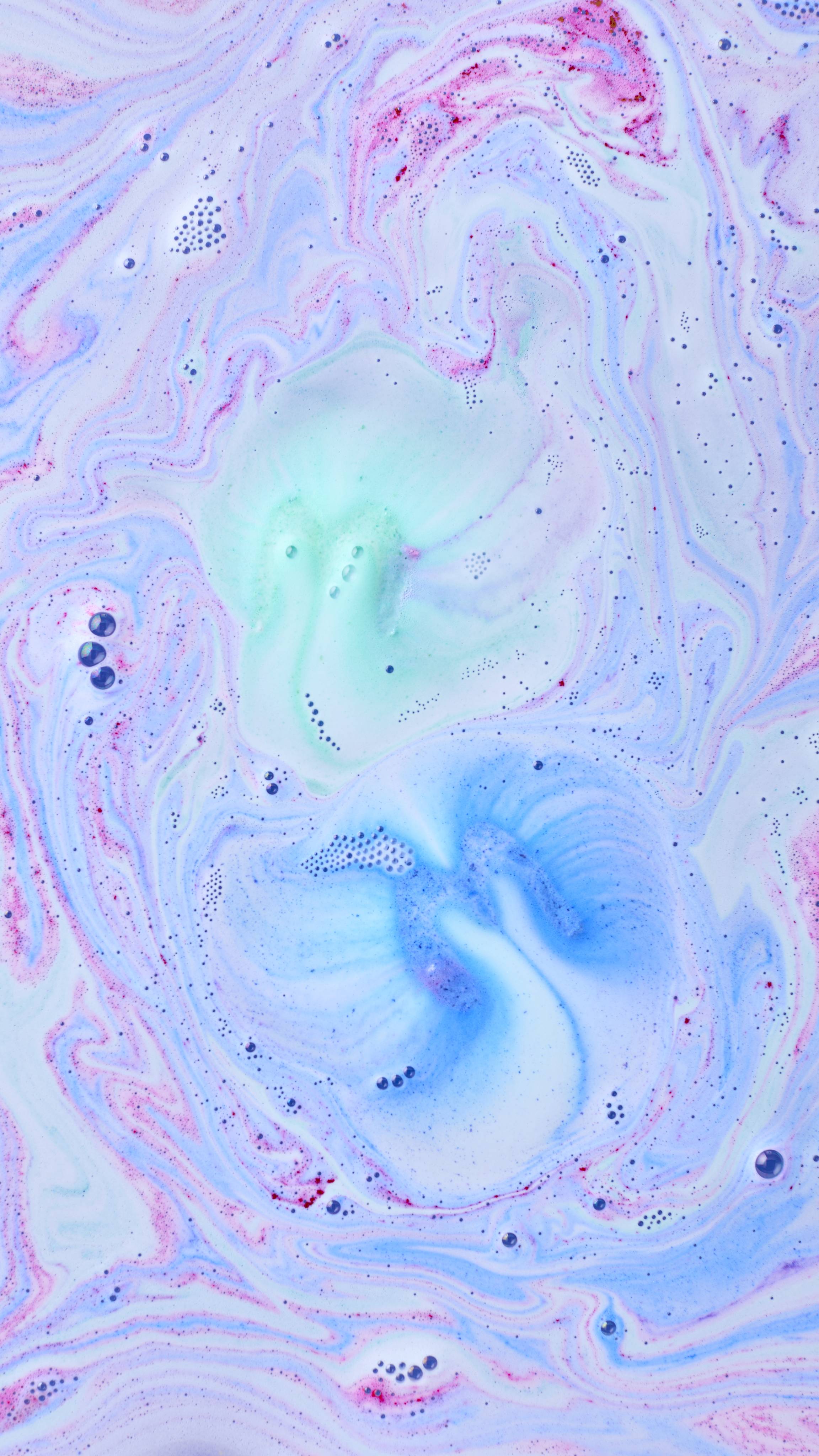 The bathwater displays a marbled effect of soft pastel colours as the bath bomb fully dissolves. Swirls of milky blue, teal, and pink foam mix together, dotted with tiny bubbles across the surface.