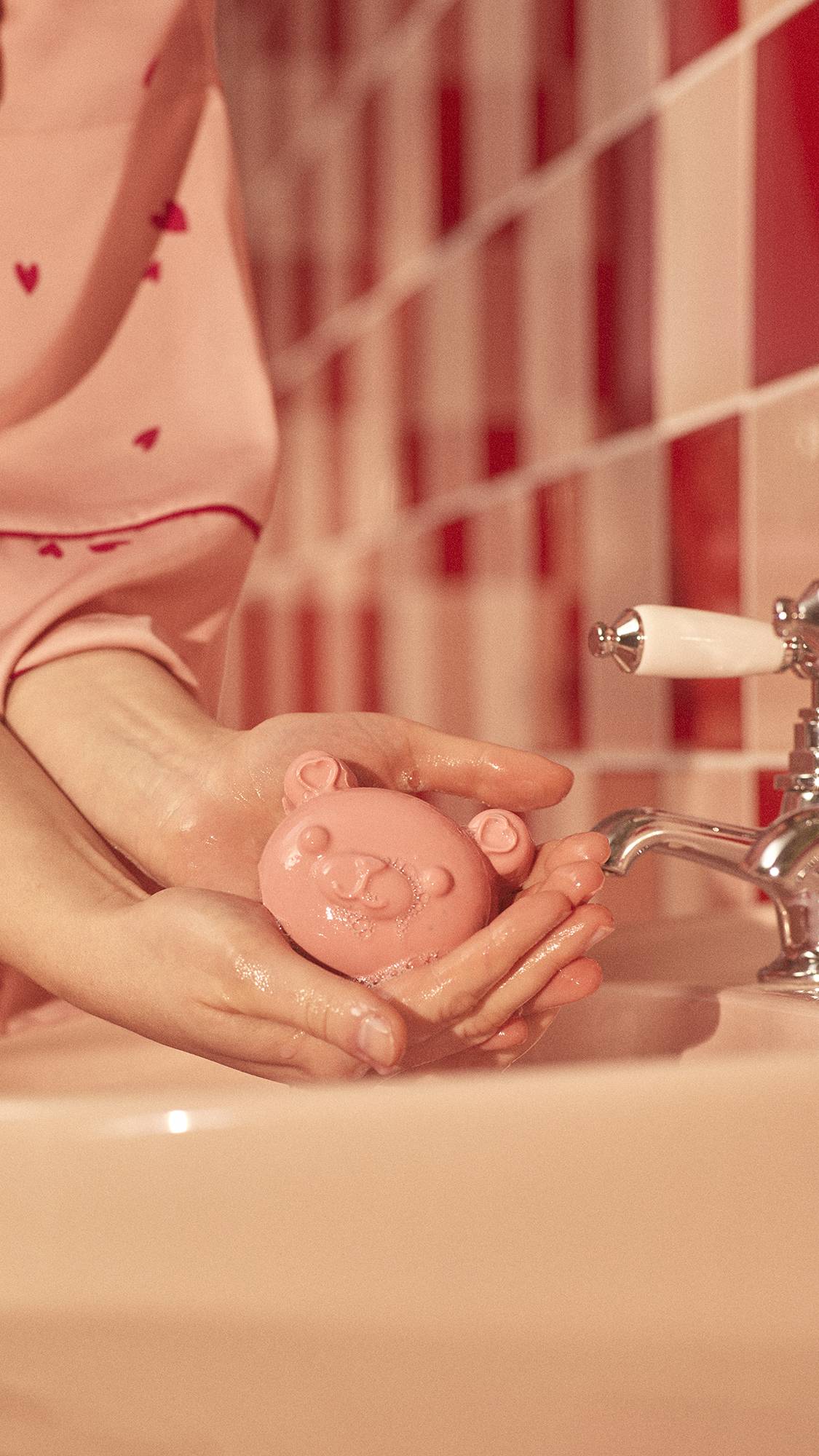 Image shows a close-up of the model's hands gently holding the My Li'l Chia Bear, dotted with soap suds, above a sink.