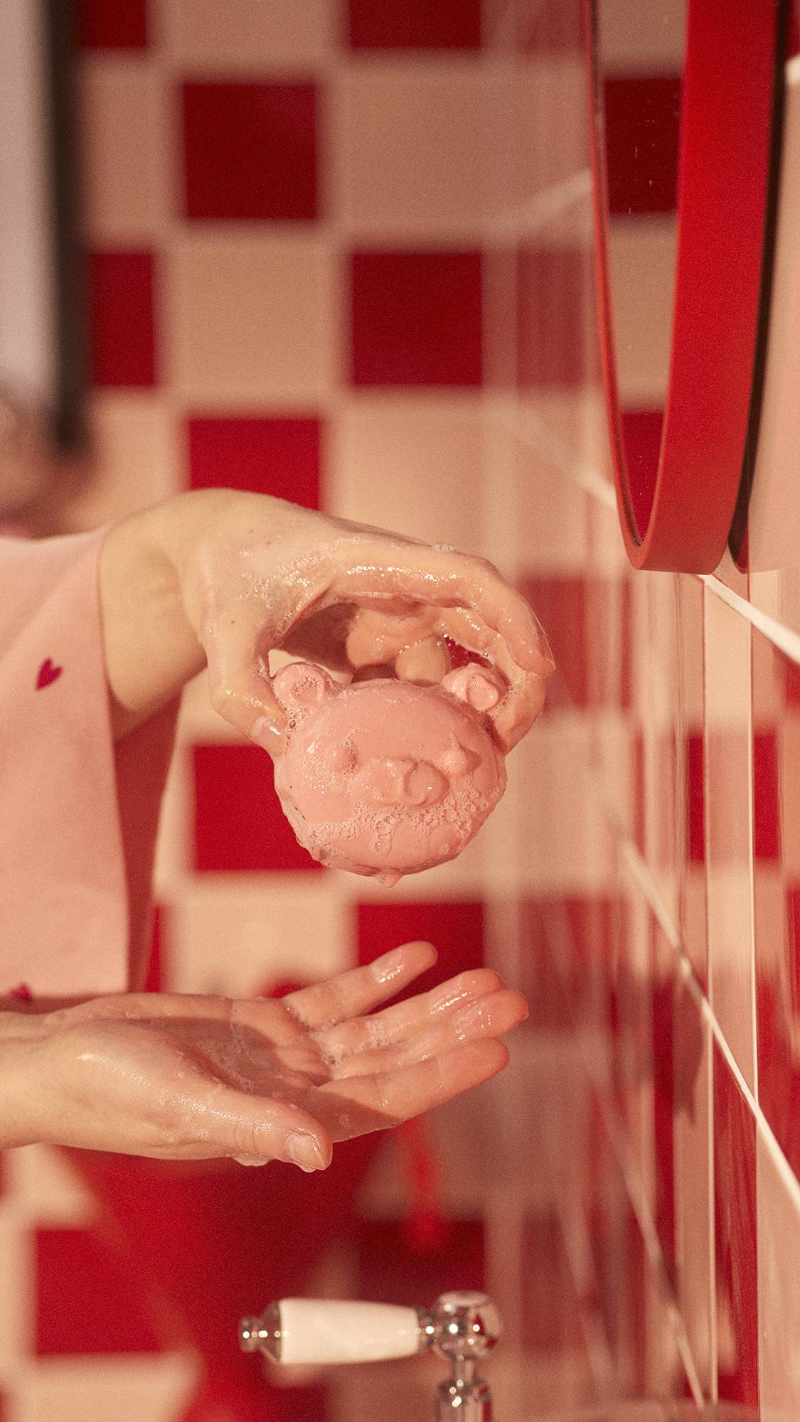Image shows a close-up of the model's hands gently holding the My Li'l Chia Bear, dotted with soap suds, above a sink.