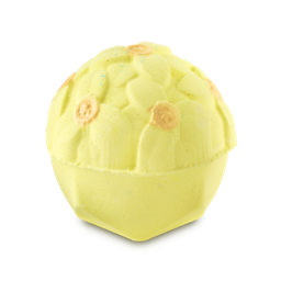 A pale yellow, dome-shaped bath bomb with a detailed floral pattern on top. Several of the molded flower centers are accented with a shimmering gold finish.