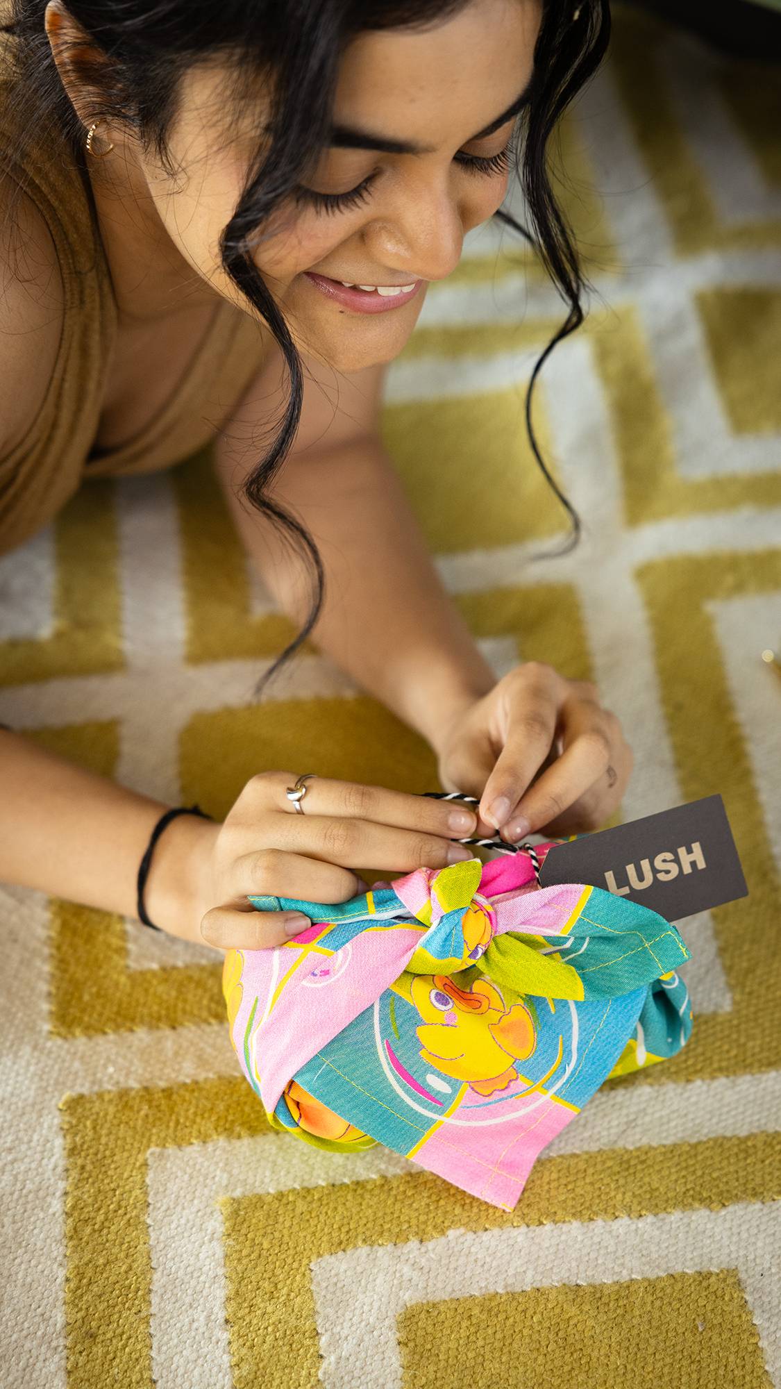 Image shows model laying down and are smiling as they finish wrapping a gift in the Nice Bath Time for Ducks knot wrap.