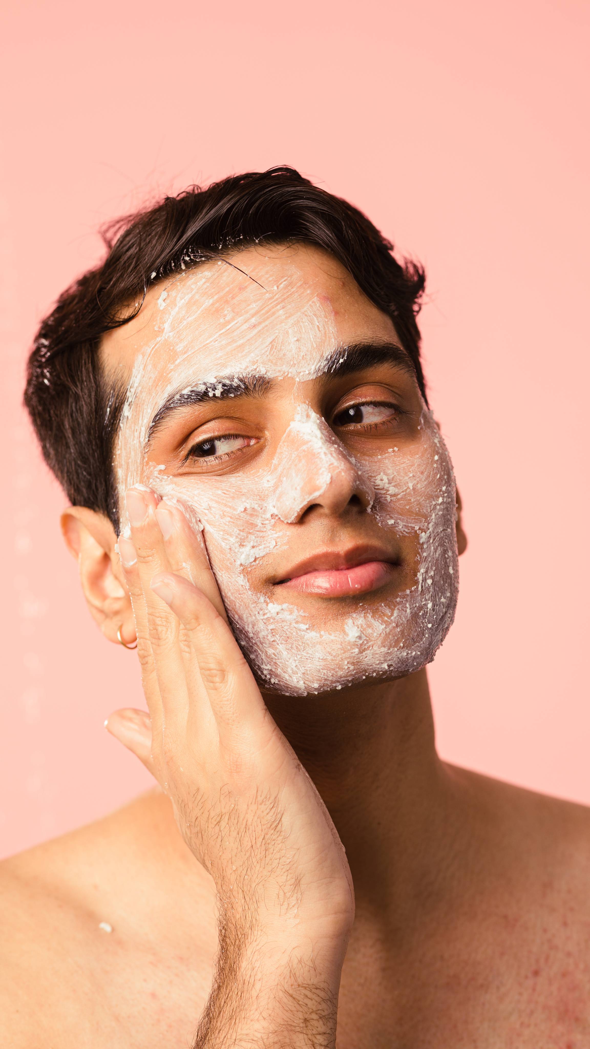 Model is using creamy face product on a light salmon-coloured background.
