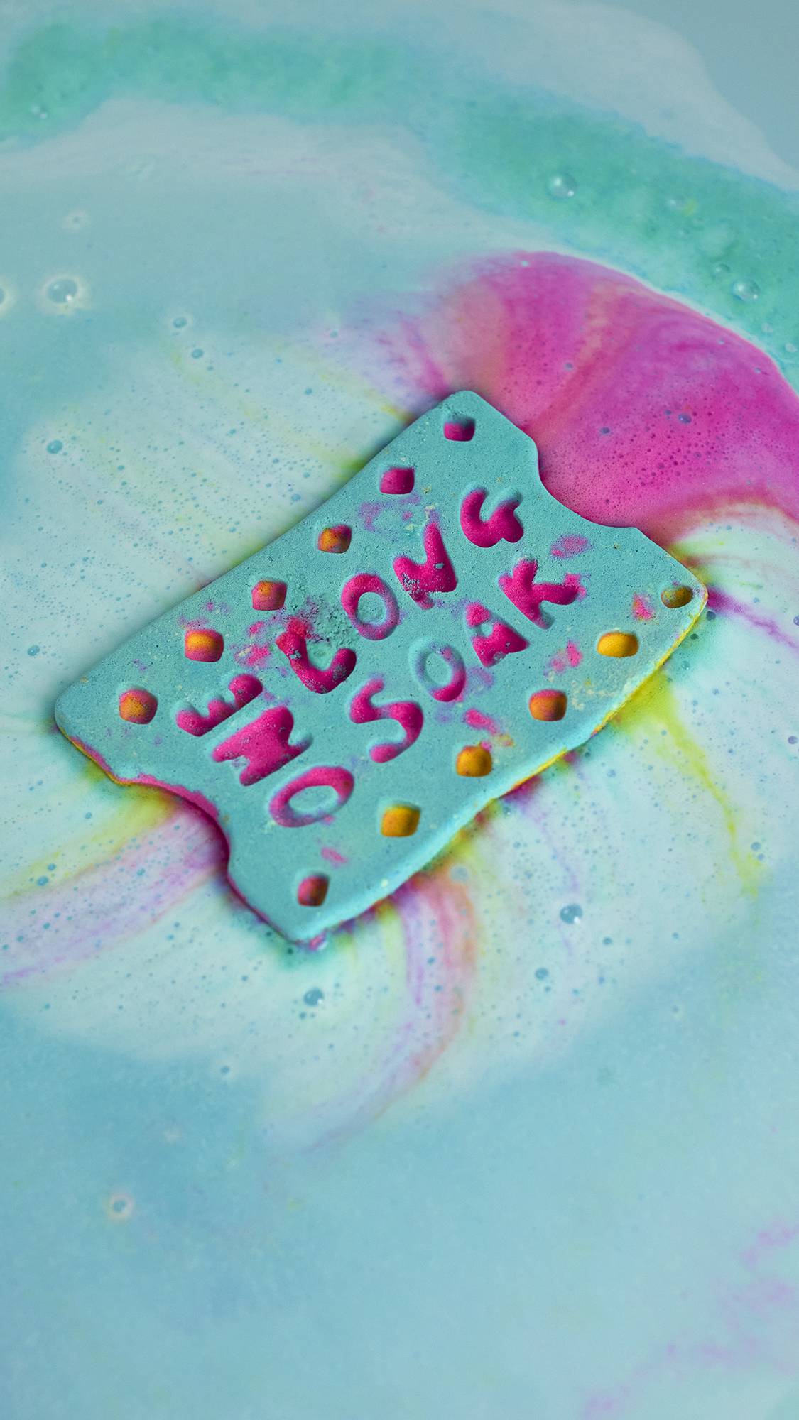 The One Long Soak bath bomb is slowly dissolving in the water giving swirls of blue, pink, and yellow.