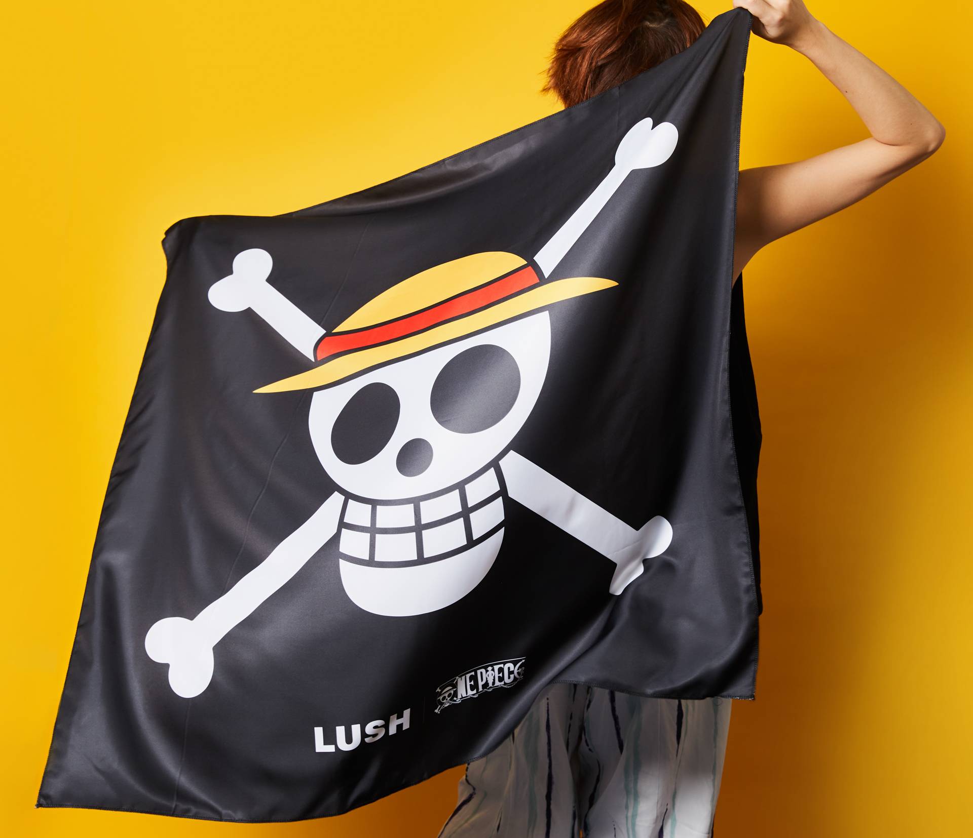 A model waves 'The Straw Hat Pirates' very own Jolly Roger Emblem designed knot wrap in front of a yellow background.
