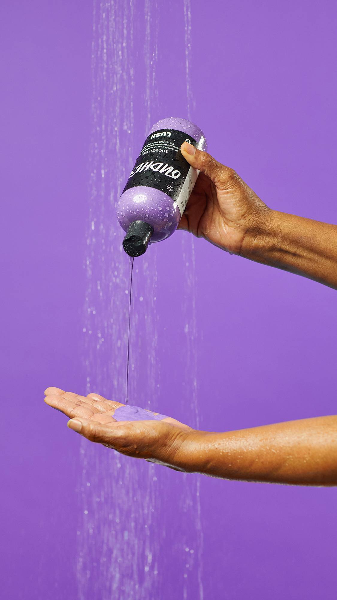A close-up of the model's hands under running as they gently squeeze the creamy, glossy shower gel from the product bottle into their open palm.