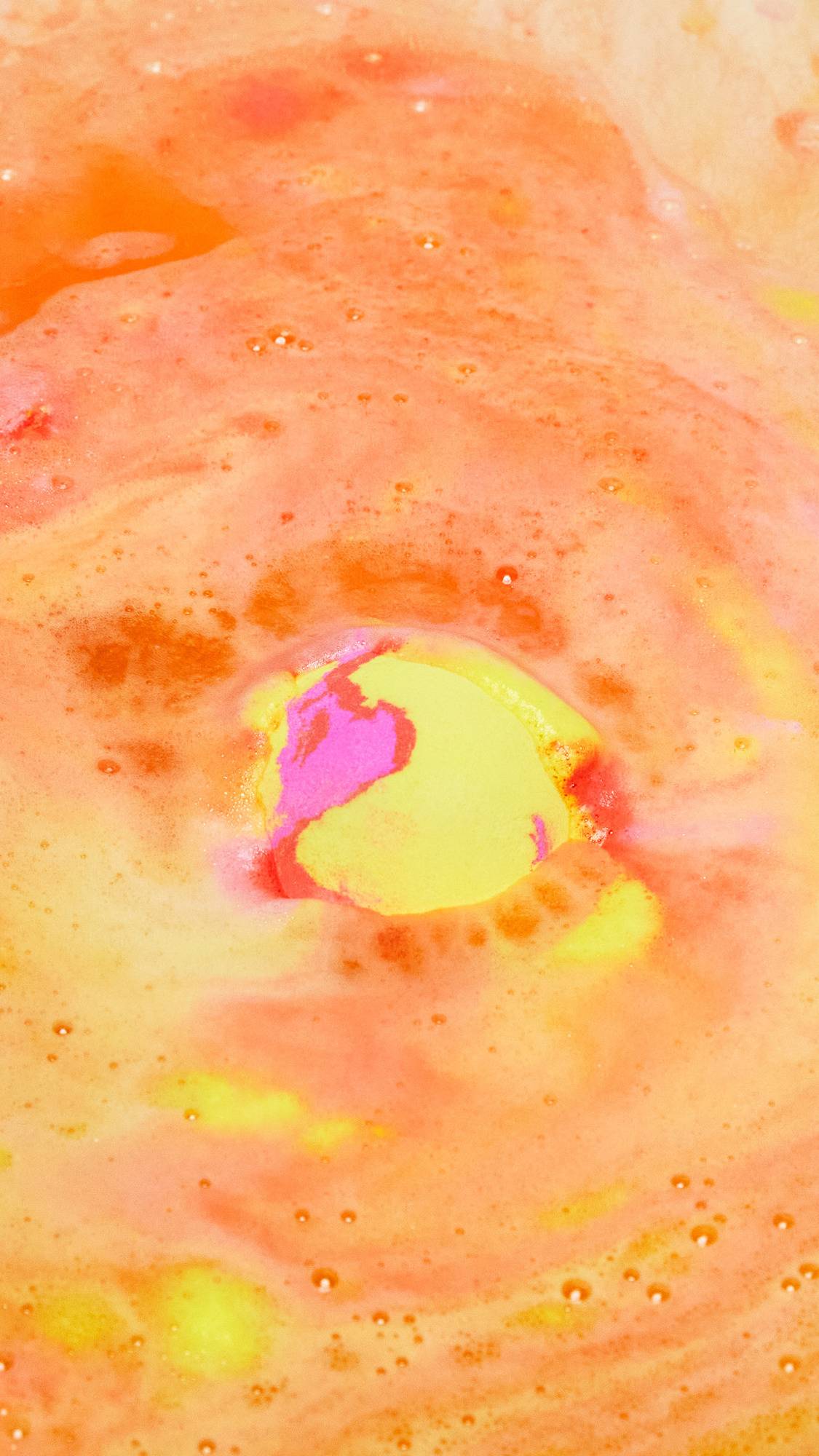 The Passion bath bomb is slowly dissolving creating swirling ripples of yellow, pink and orange. 