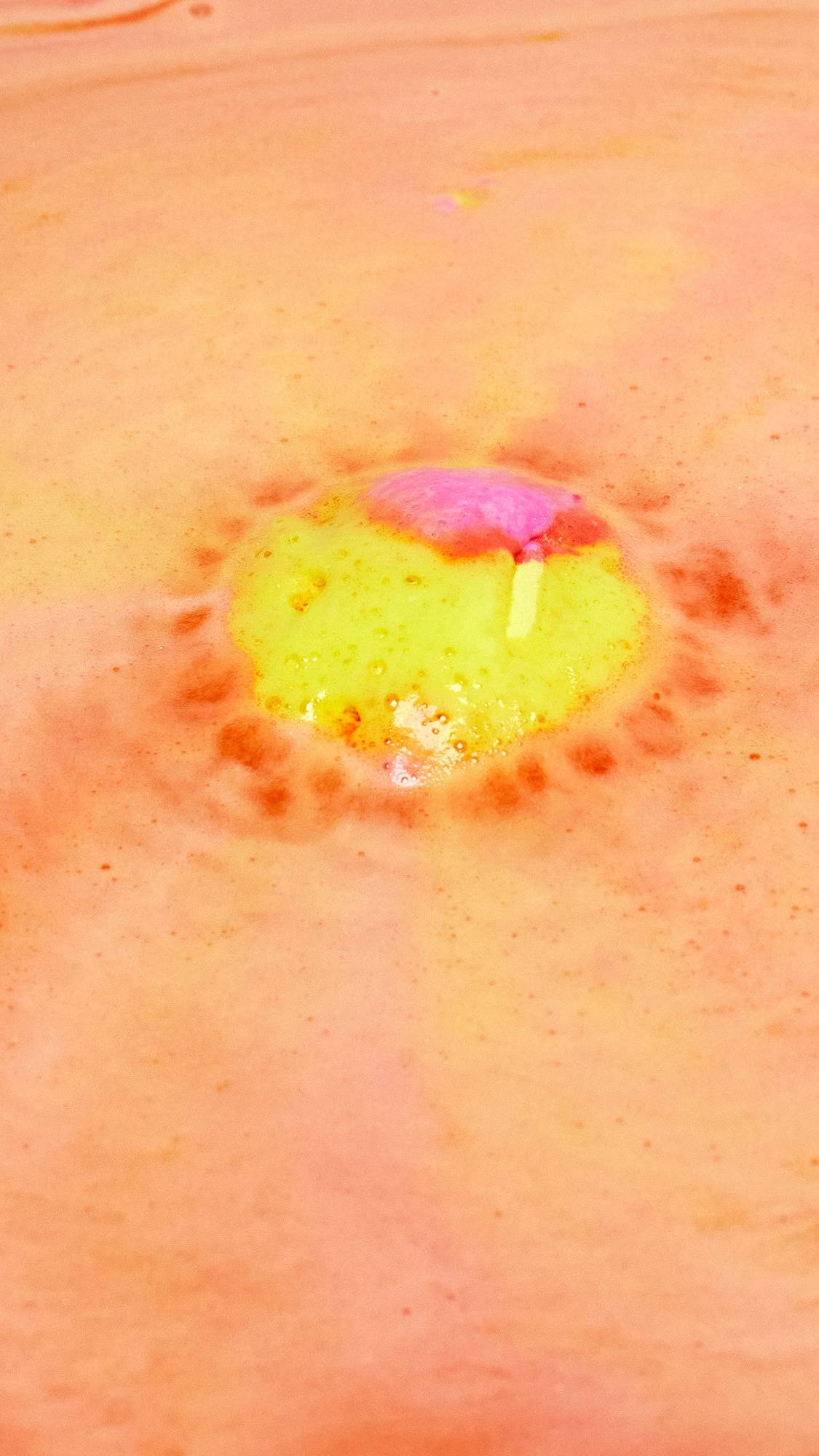 The Passion bath bomb is slowly dissolving creating swirling ripples of yellow, pink and orange with a bright burst of yellow in the centre.