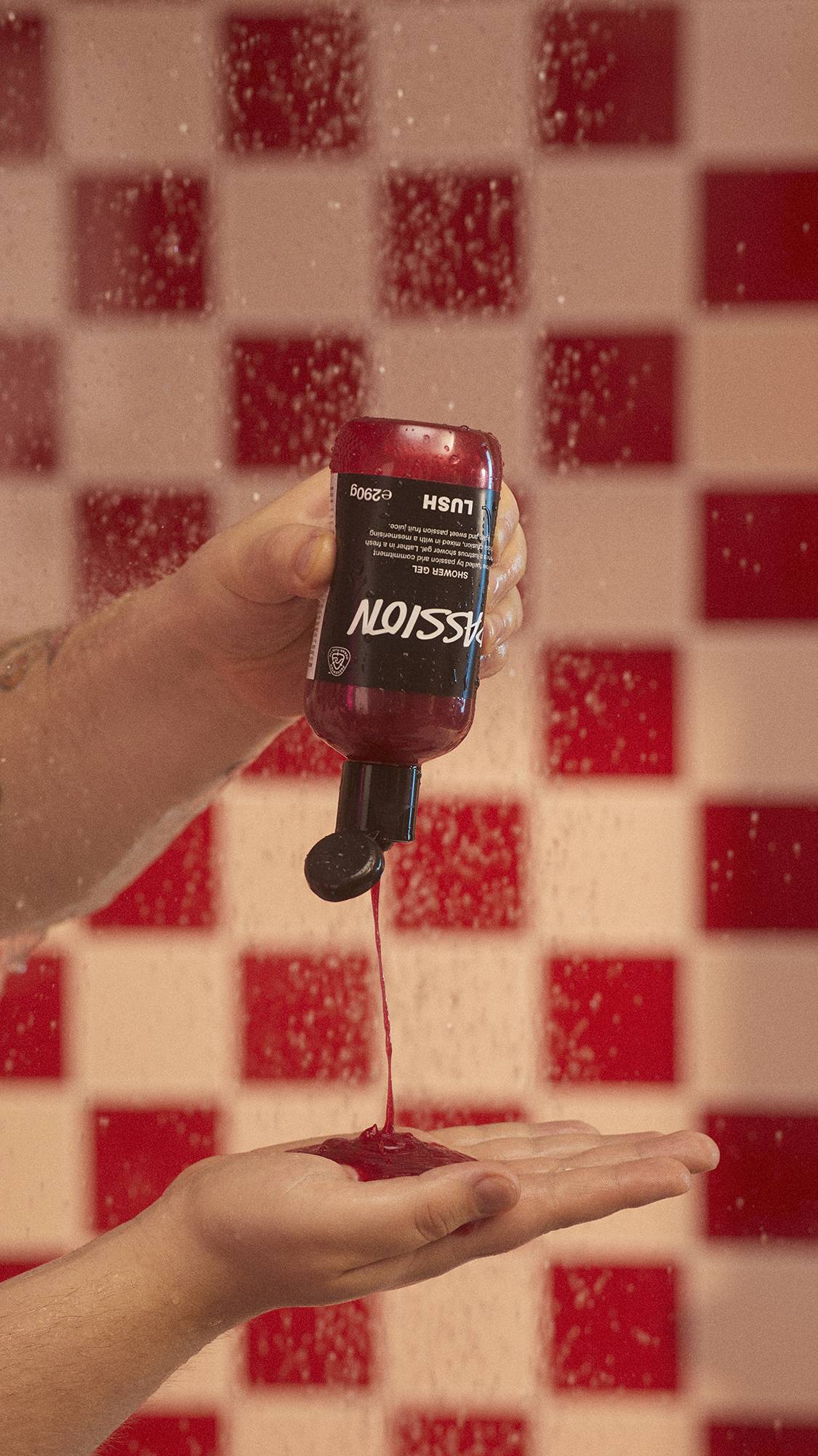 A close-up image of the model squeezing the bottle of Passion shower gel into their hand under running shower water.
