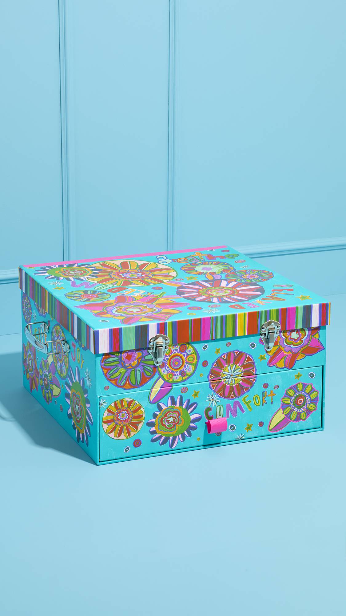 A large, light blue trunk from the Peace and Love gift set. It features vibrant floral illustrations, metal latches on the lid, and a front drawer labeled 'COMFORT' with a pink pull tab.