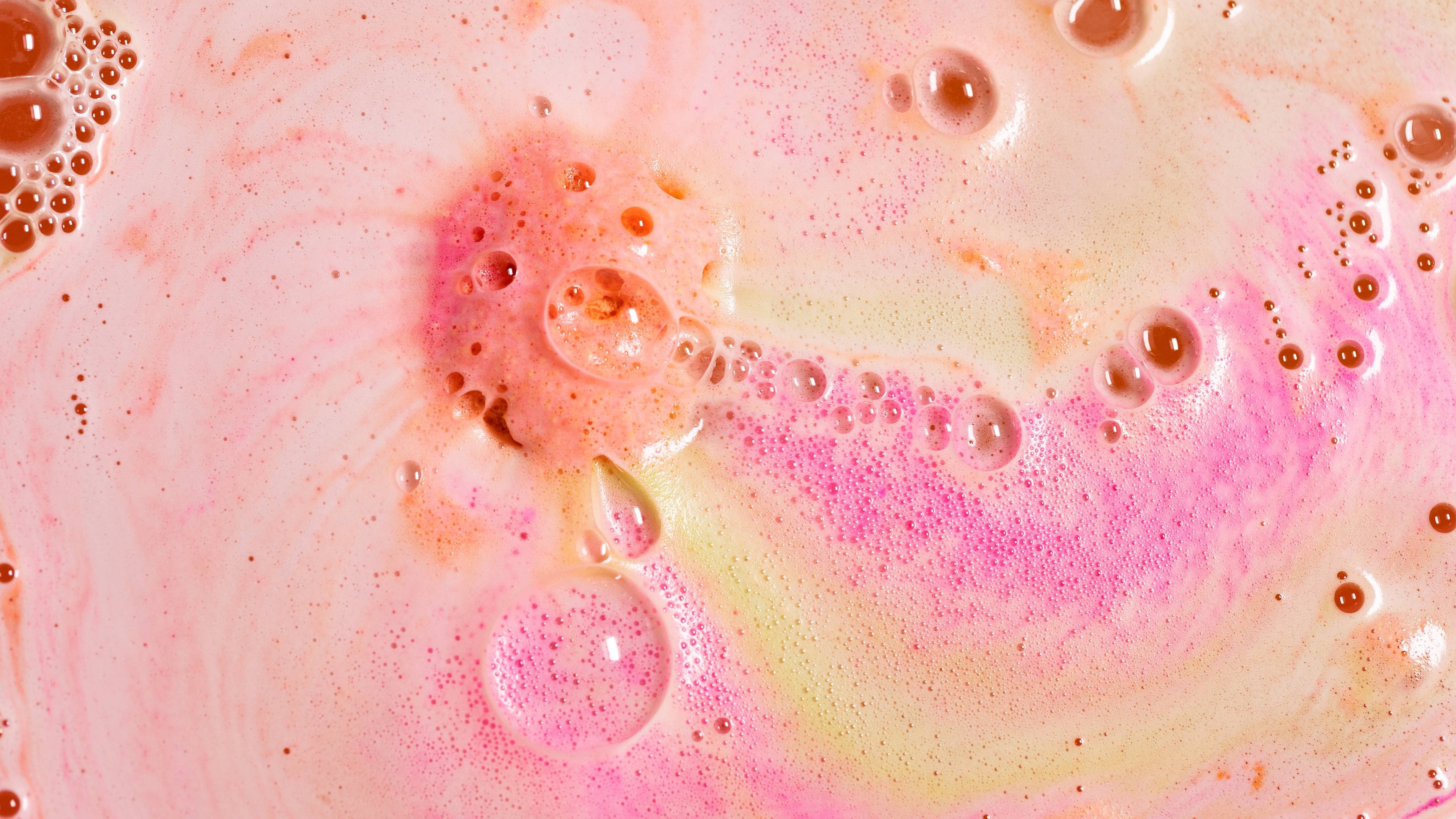 Close-up of Peachy bath bomb in the tub. Pink and coral-coloured froth and bubbles.