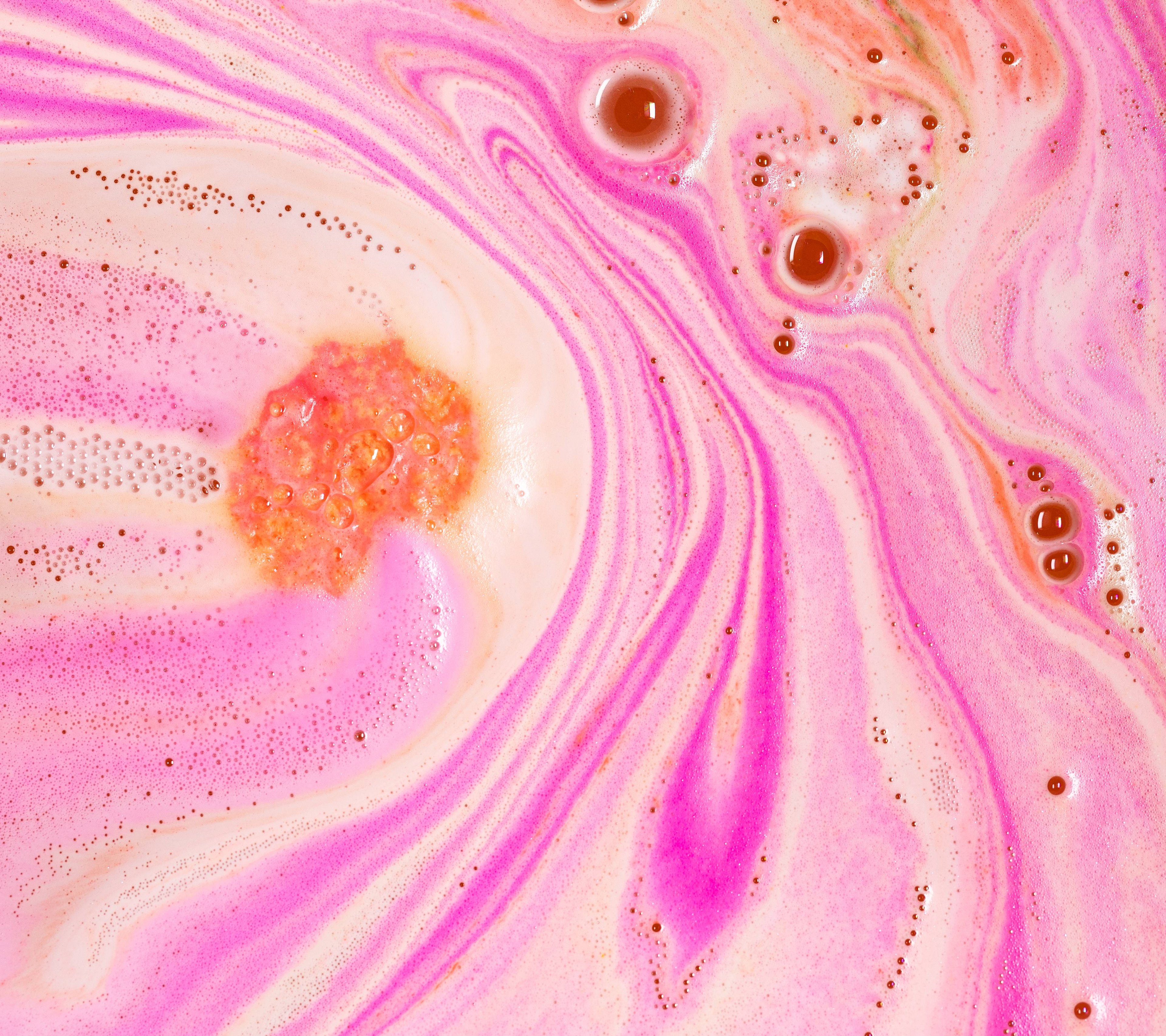 A close-up of a submerged Peachy bath bomb with a peachy pink, orangey foam and large bubbles. 