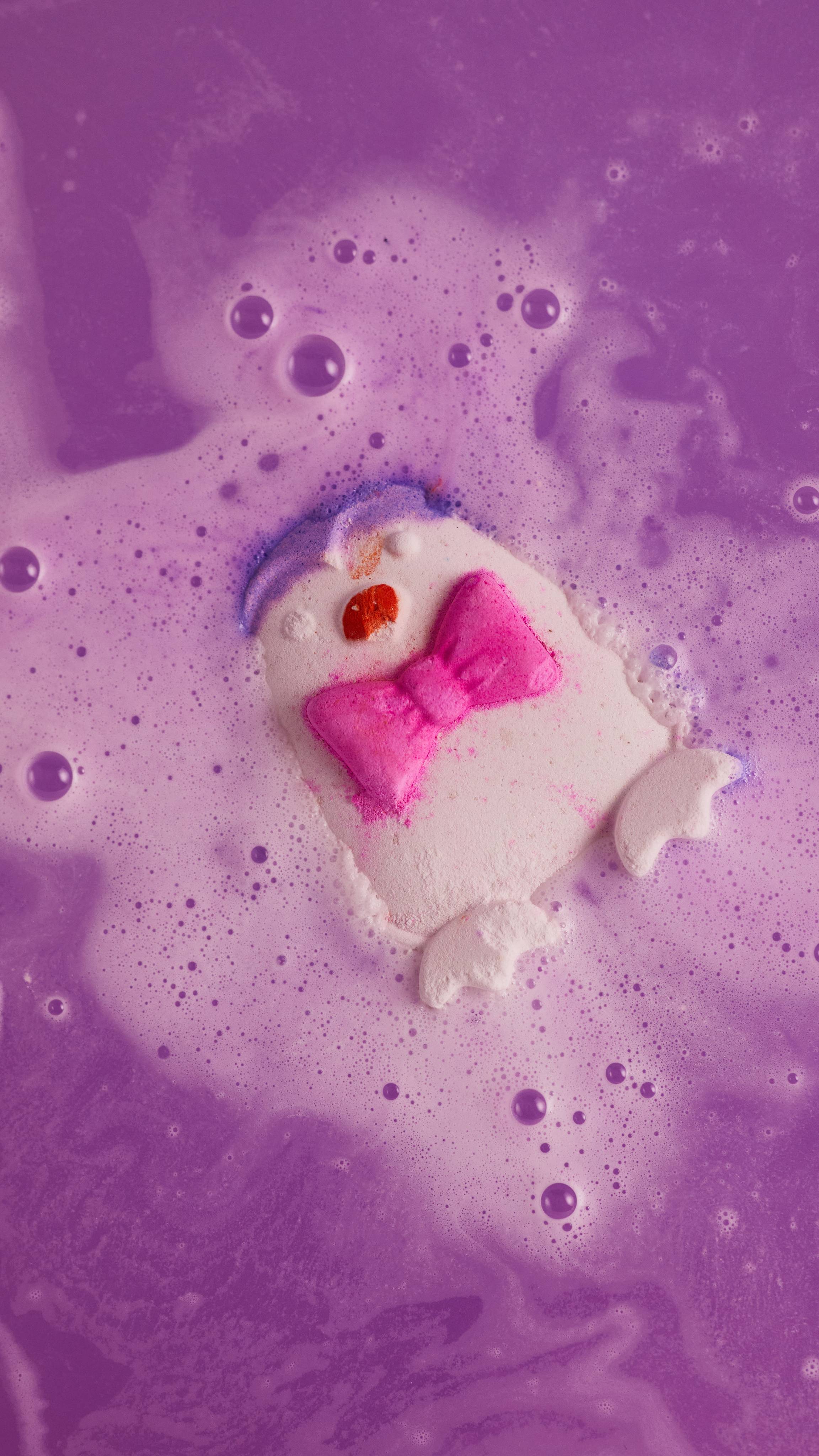 Penguin bath bomb begins to fizz away in the bath water giving off twirls of lavender coloured foam.