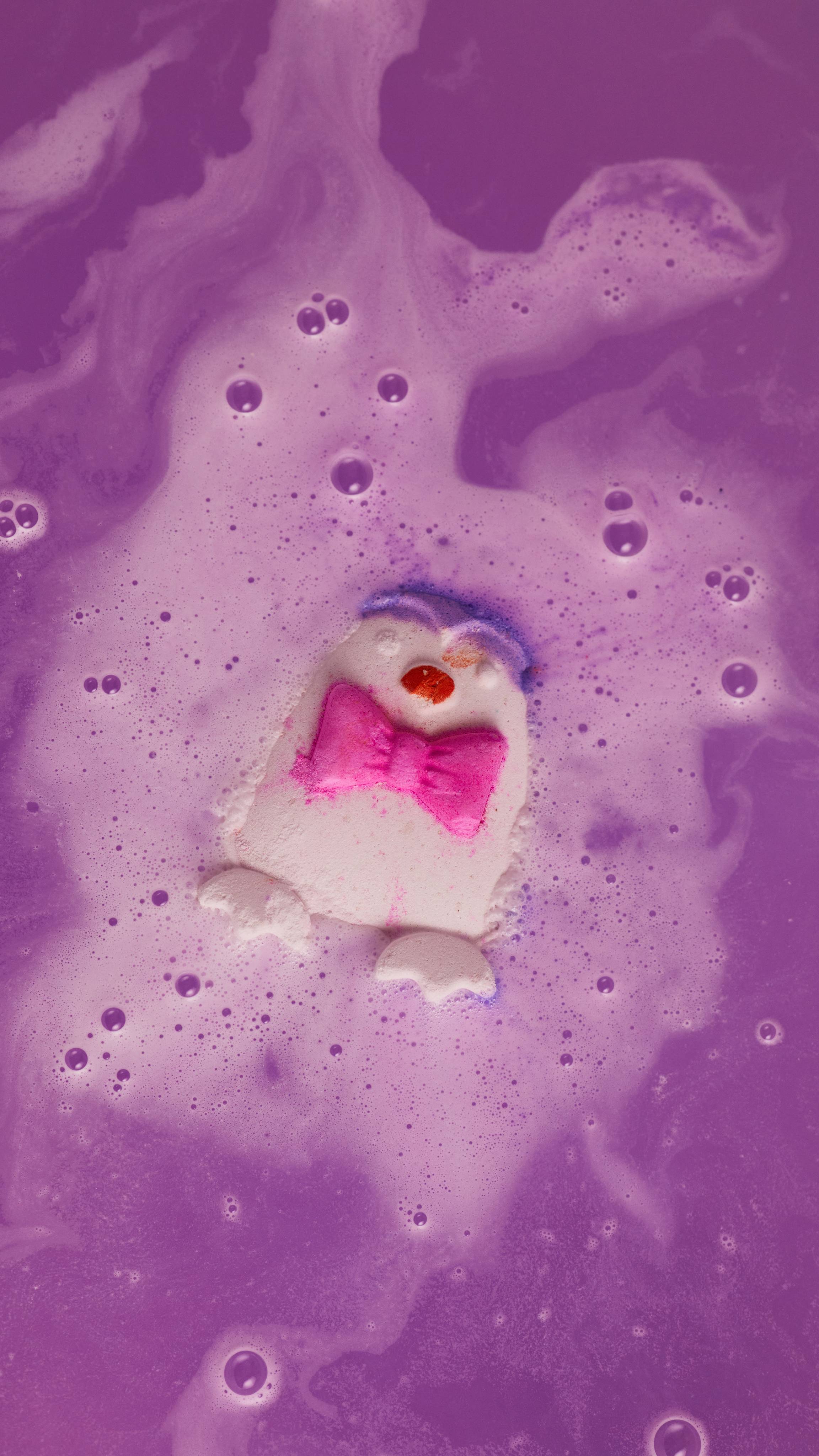 Penguin bath bomb begins to fizz away in the bath water giving off twirls of lavender coloured foam.