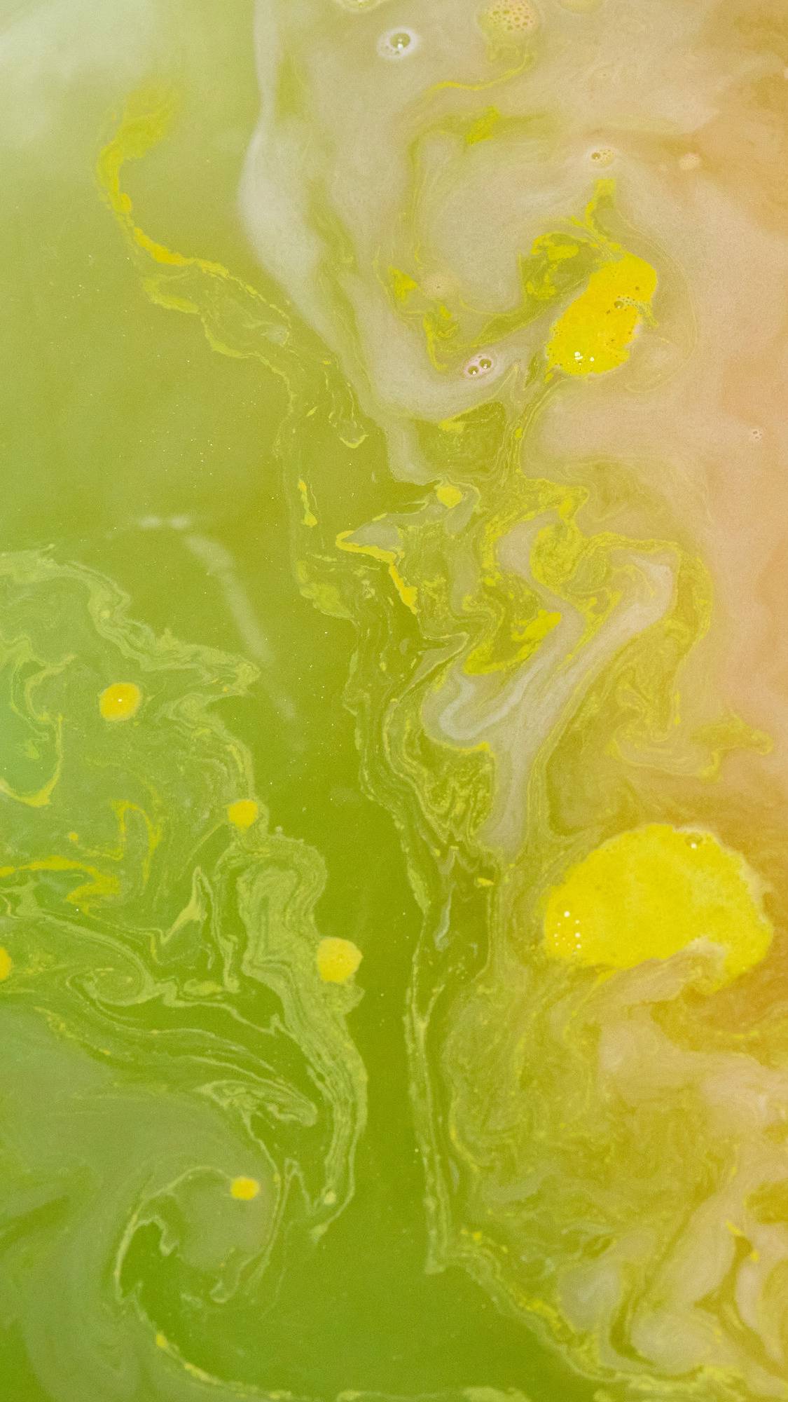 The image shows a close-up of the bath water after using the Pig In A Poke bath bomb. The water is a vibrant yellow with rippled swirls of even brighter yellow. 