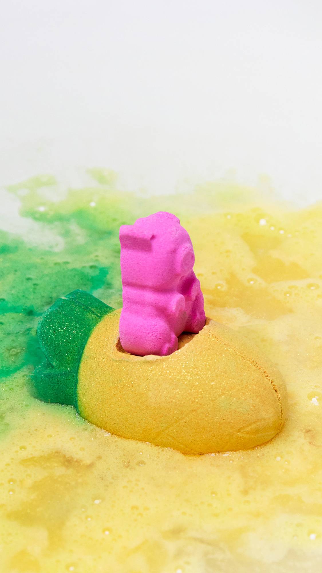 The Pig In A Poke bath bomb is sitting perfectly on the bath water as it gives off a blanket of vivid yellow and green swirling foam. 