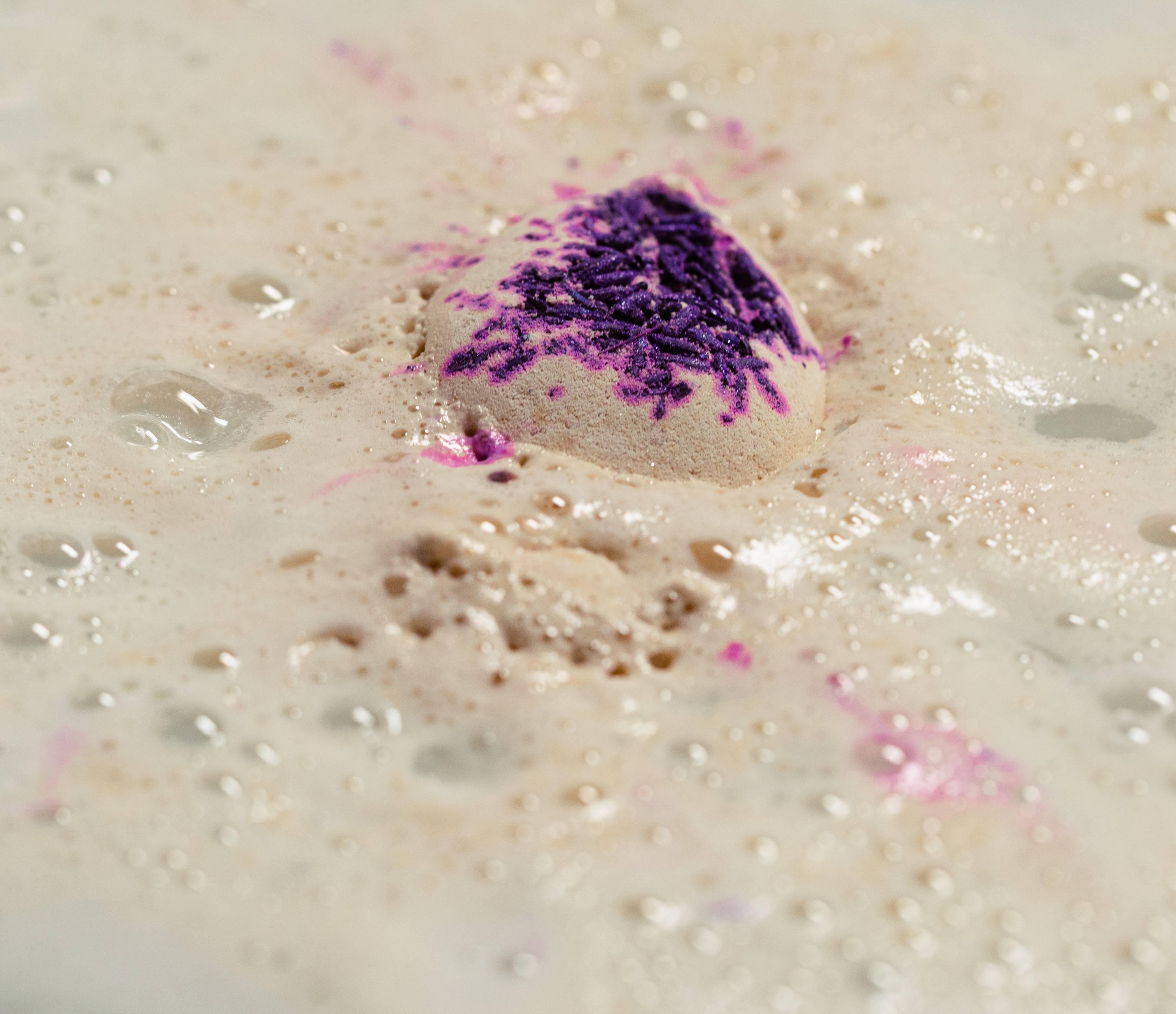 Image shows the Sleep Bear bath bomb nearly dissolved with small flecks of purple and lavender flowers sit on top.