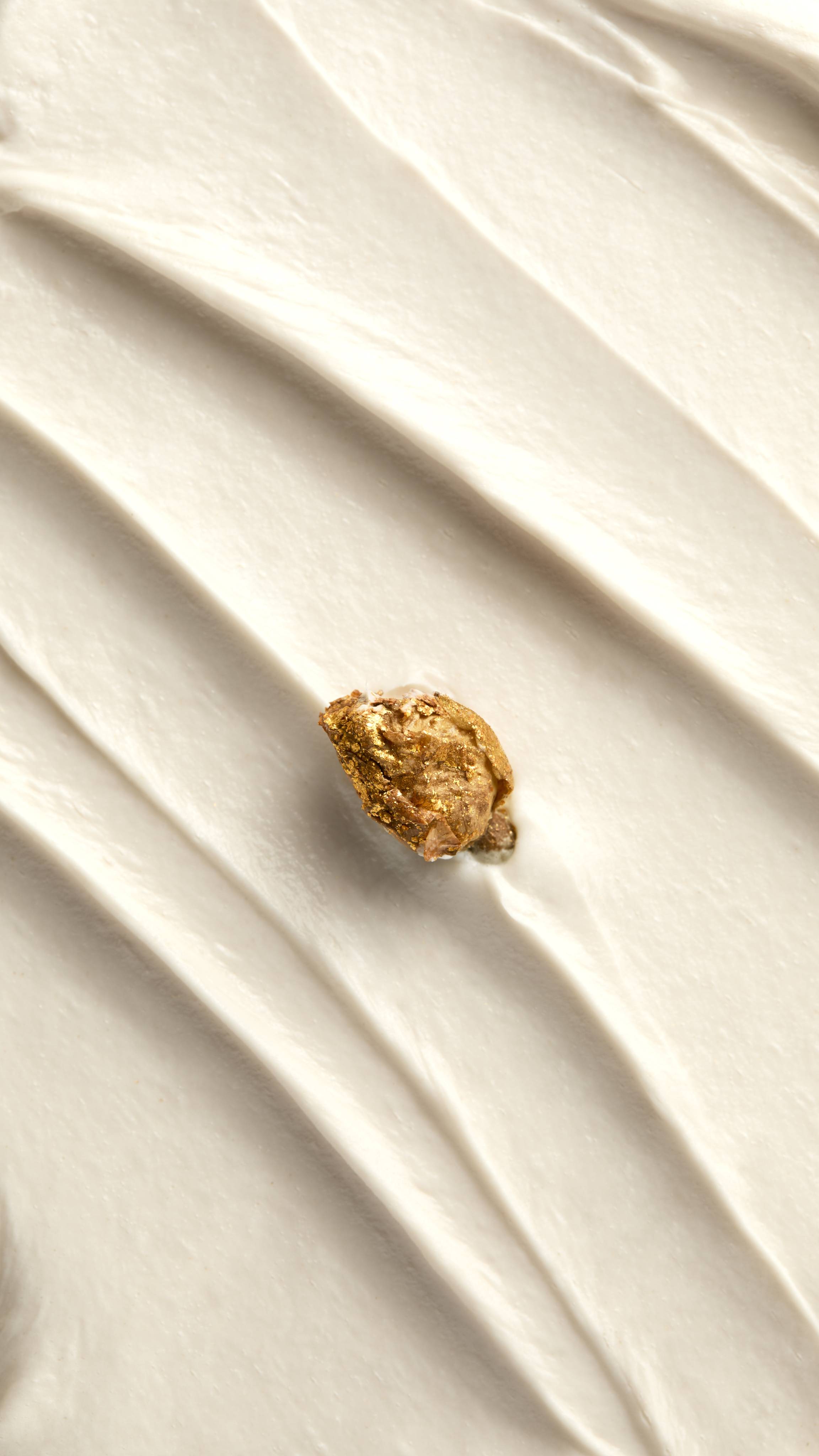 A close-up shot displays the thick, creamy white texture of the "Posh White Chocolate and Rose" body wash, spread into diagonal ridges. A single dried rose bud, dusted with gold shimmer, rests in the center of the mixture.