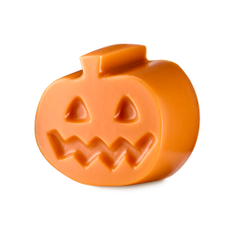 A solid orange Lush pumpkin facial gummy against a white background. The smooth, chunky jack-o'-lantern figurine features small carved triangular eyes and a wide, zigzagging smile on its front surface.