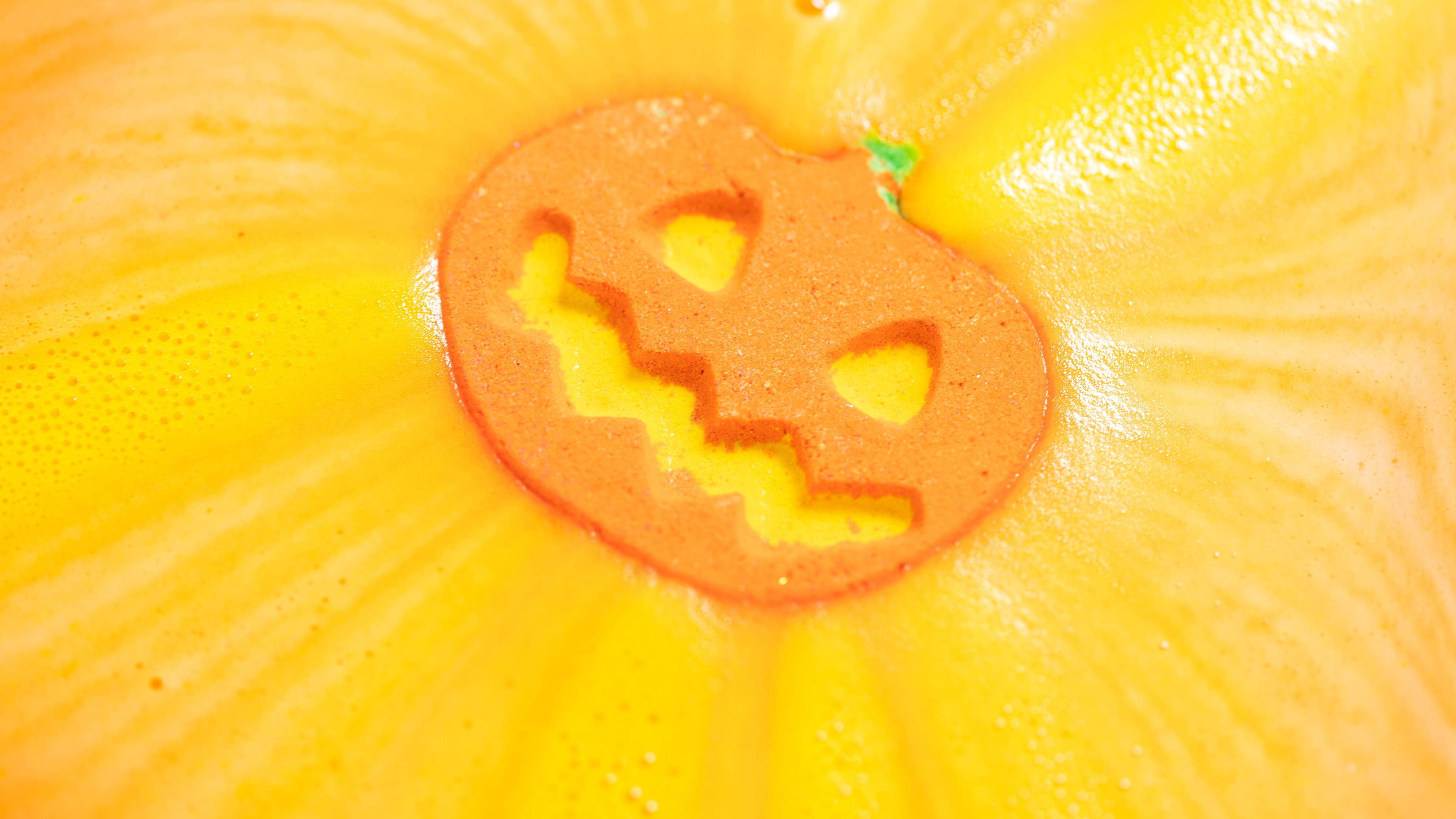 The Punkin Pumpkin bath bomb fizzes in water, releasing bright orange and yellow foam across the surface.