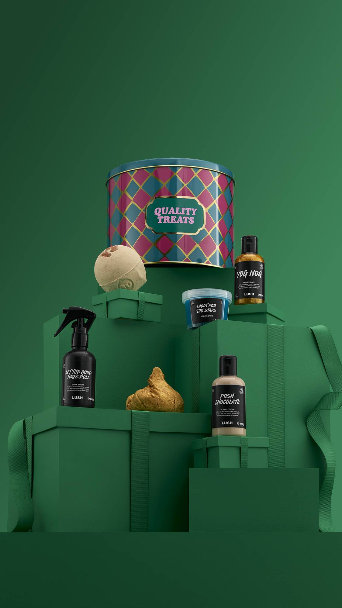 The image shows a large pile of differently-sized wrapped green gifts with ribbons, on a matching green background. The colourful "Quality Treats" gift tin sits on top of the pile, and the six included products sit on lower green gifts. 