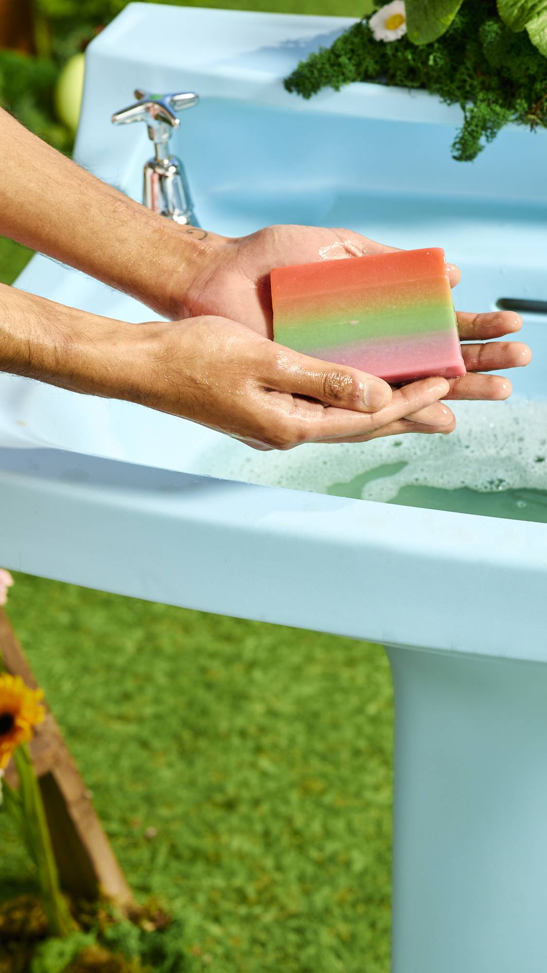 A close-up of the model holding the Rainbows and Waterfalls soap with both hands above a pale blue sink.