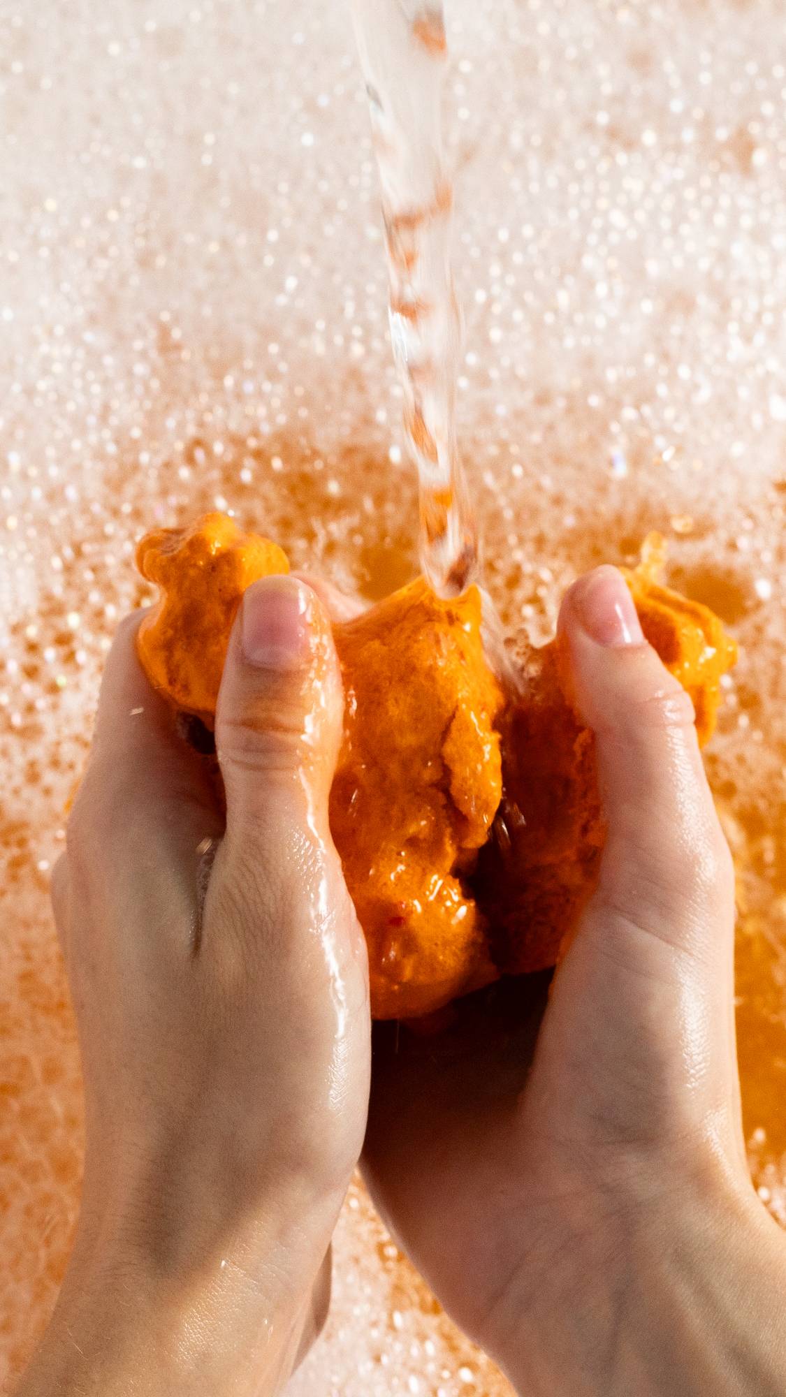 Image shows model crumbling the Reindeer bubble bar under running water as orange bubbles form in peaks below.