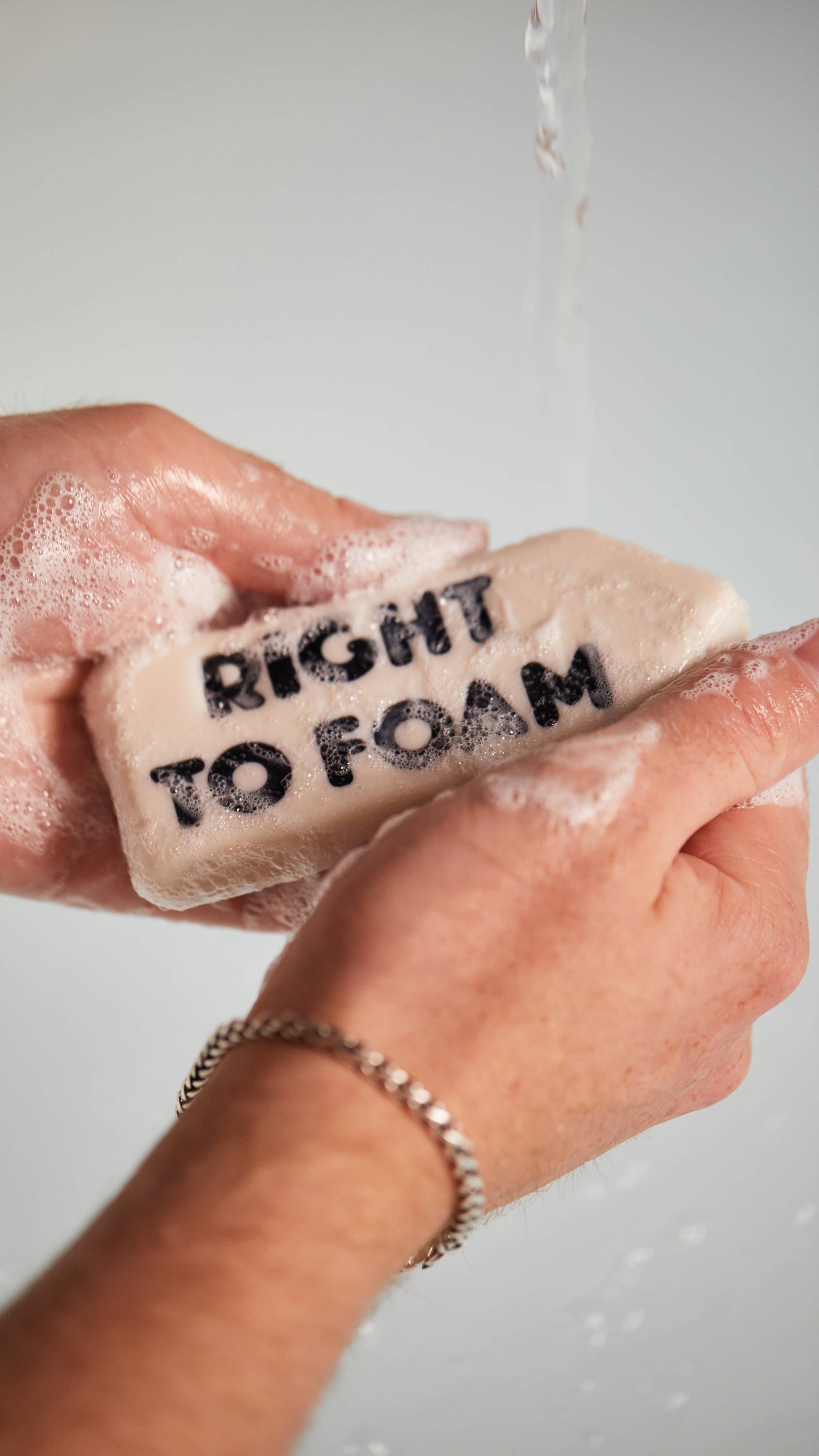 Image shows a close-up of the model's hands as they create a lather with the Right to Foam soap under running water.
