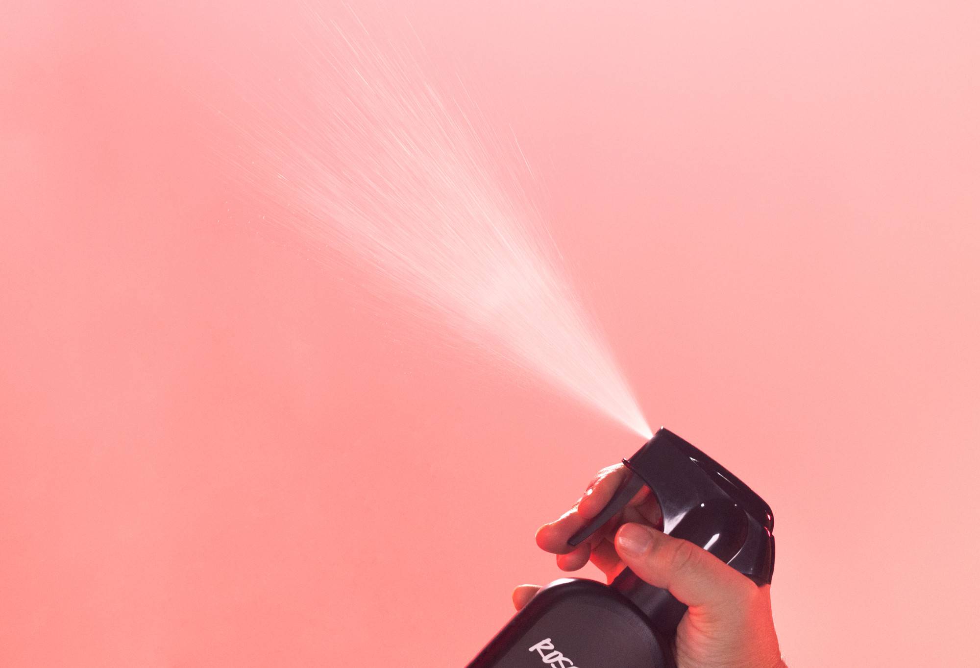 Rose Jam body spray is sprayed up into the air, in front of a vibrant, rosy pink background.
