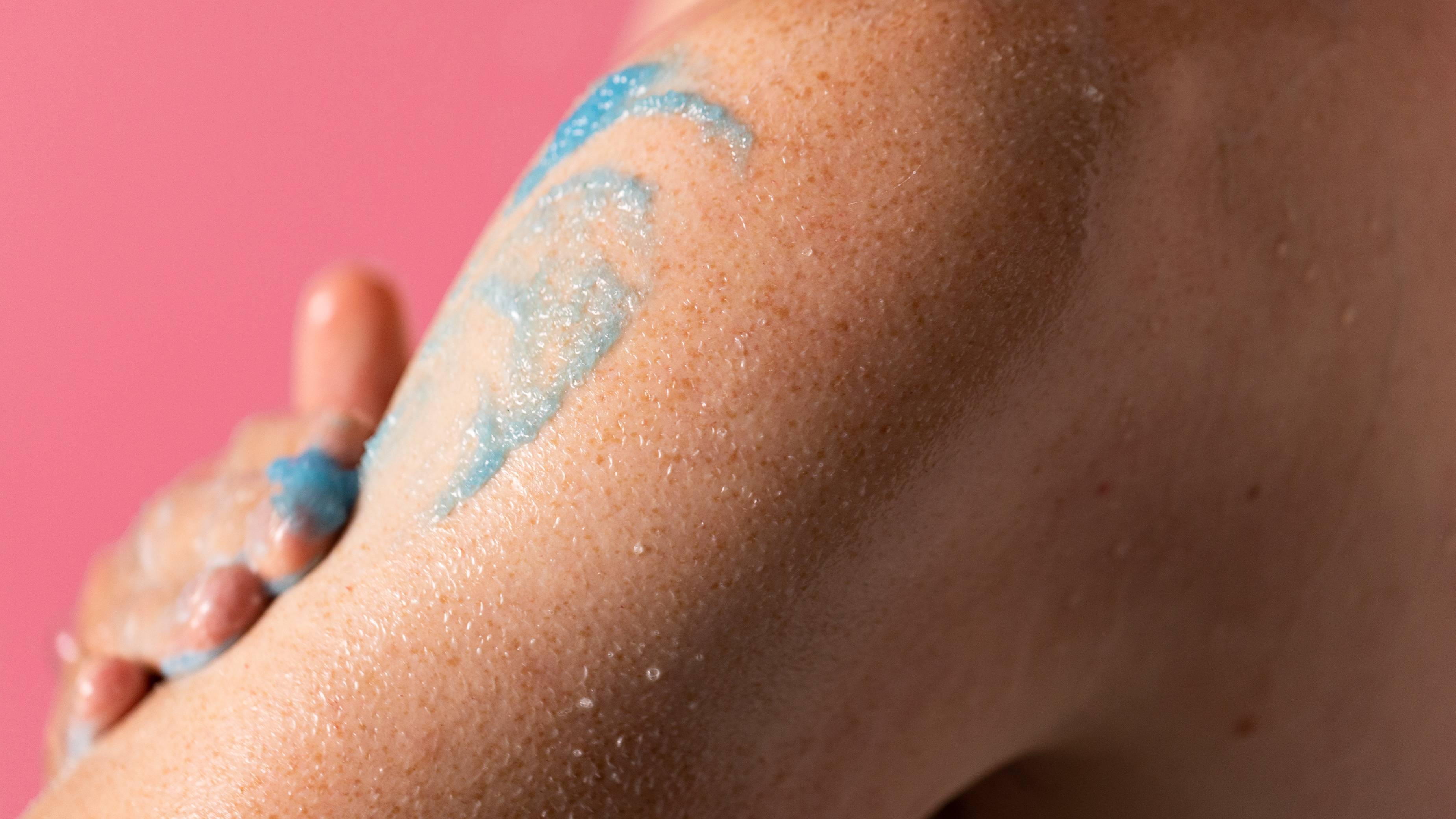 The image shows a close-up of the model exfoliating their skin with the blue, Rub Rub Rub body scrub. 