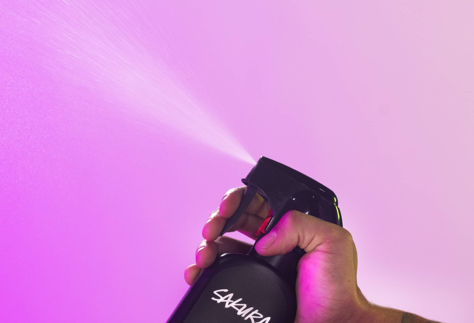 Sakura body spray is sprayed up into the air, in front of a vibrant, light purple background.